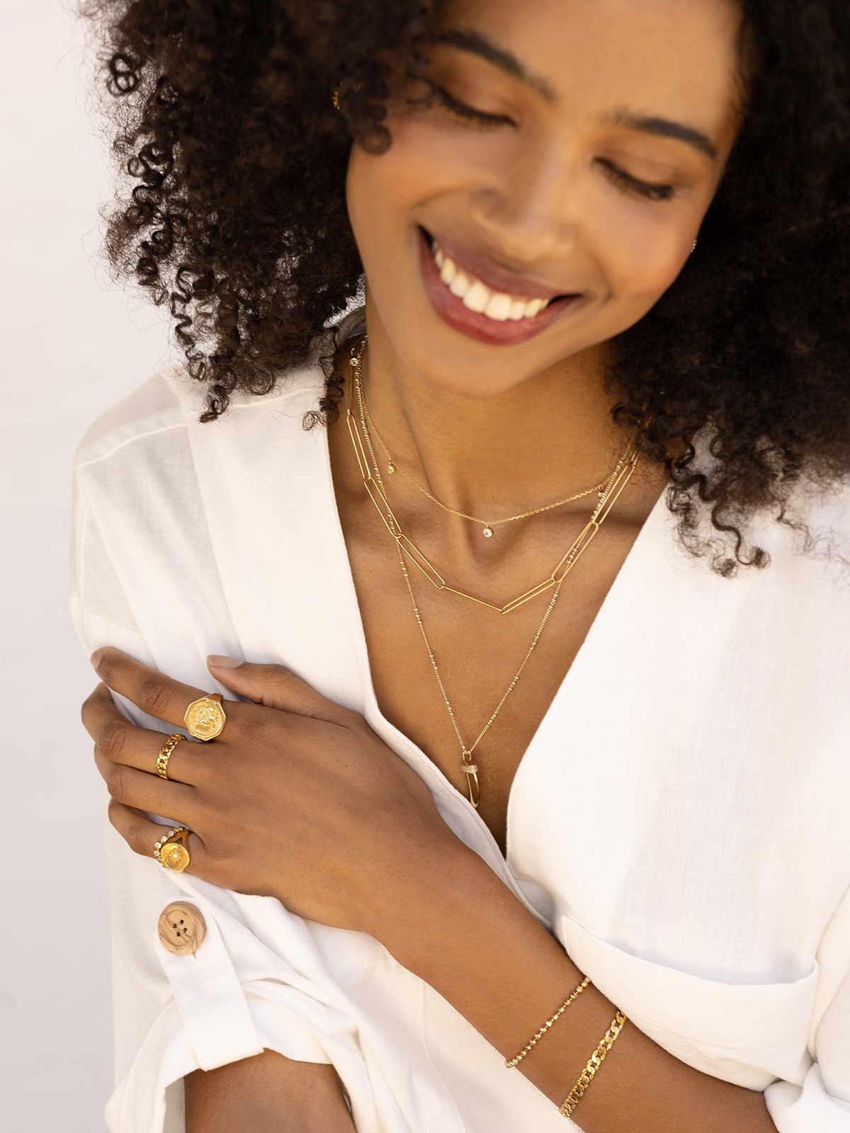 Smiling model in a white blouse wearing layered necklaces and bracelets