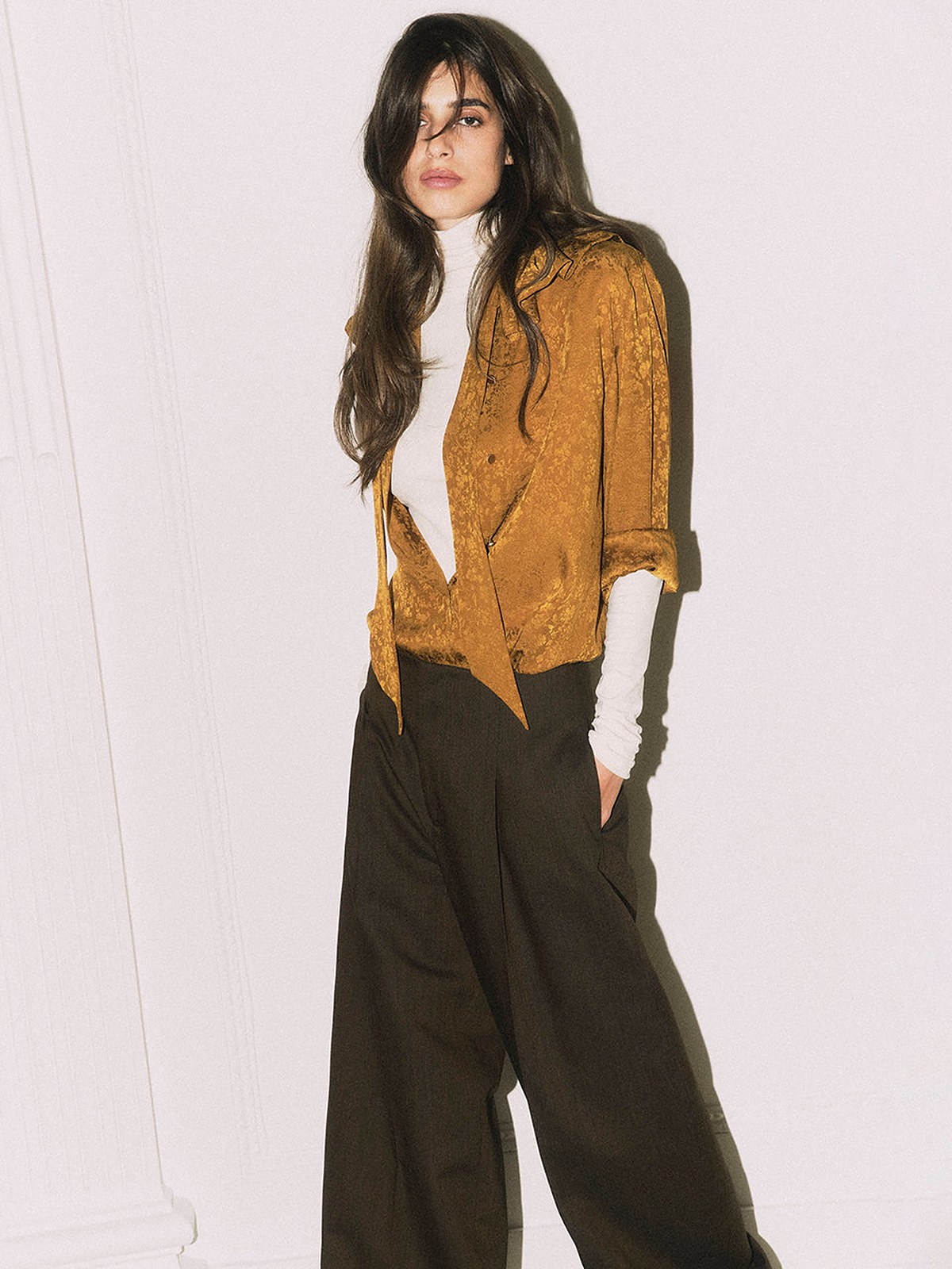 Model in an ochre silk blouse and wide black trousers