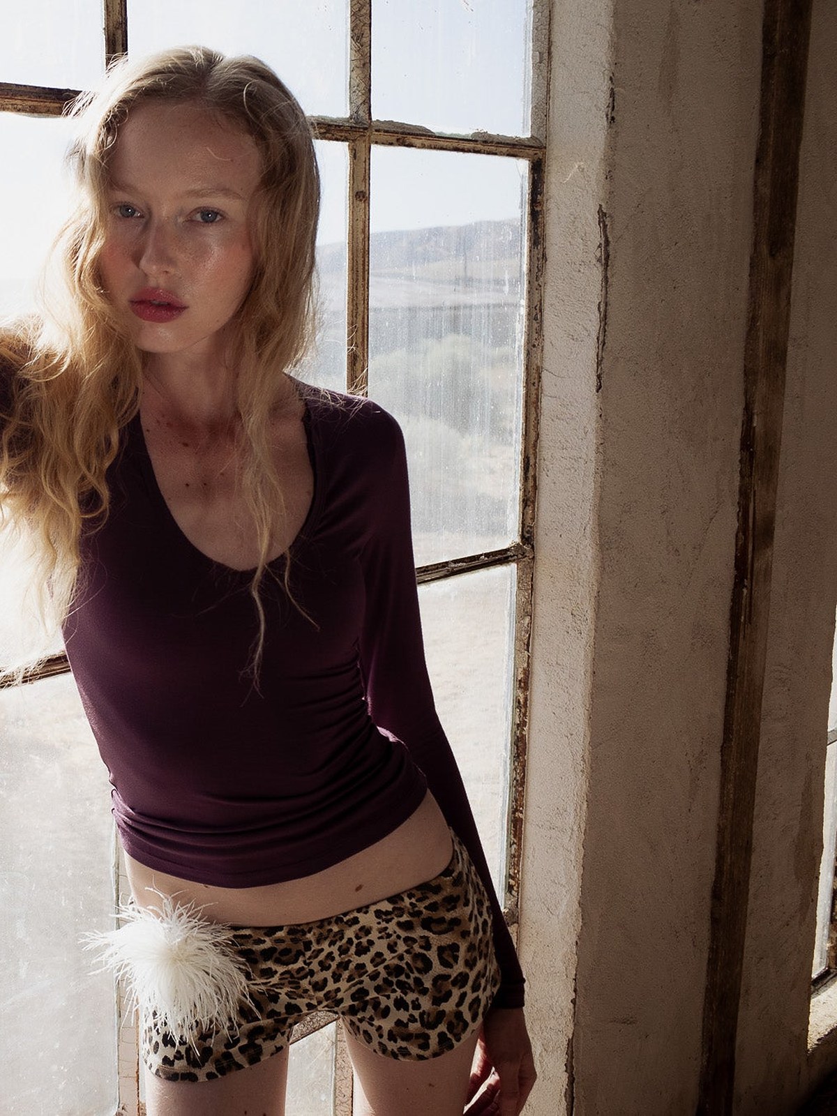 Model in a plum fitted top and leopard print shorts leaning in a window frame