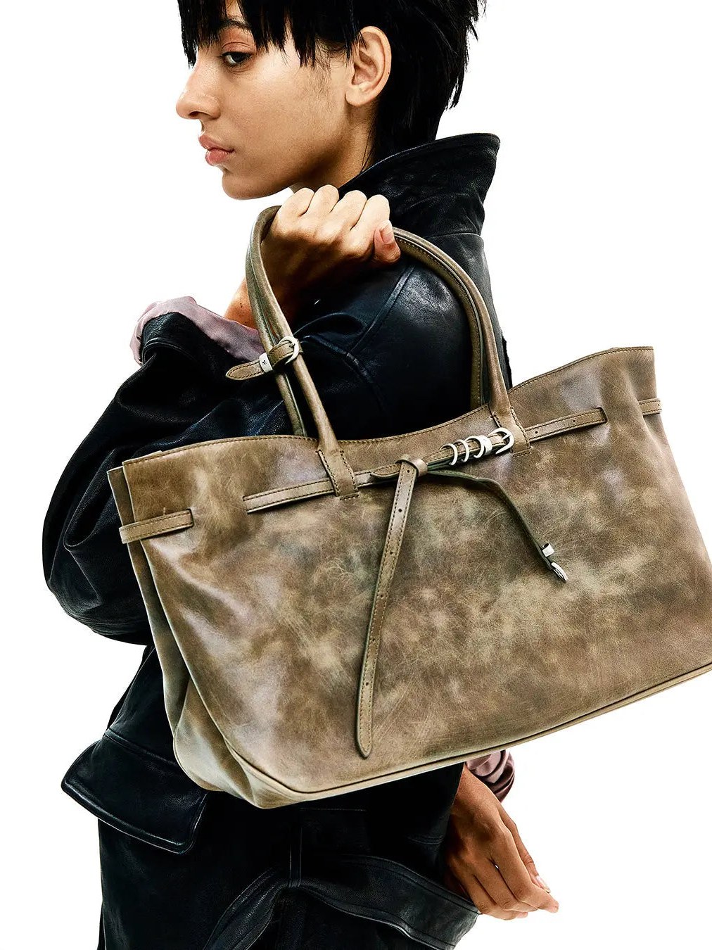 Model in dark leather holding a neutral MARGESHERWOOD tote in a styled studio