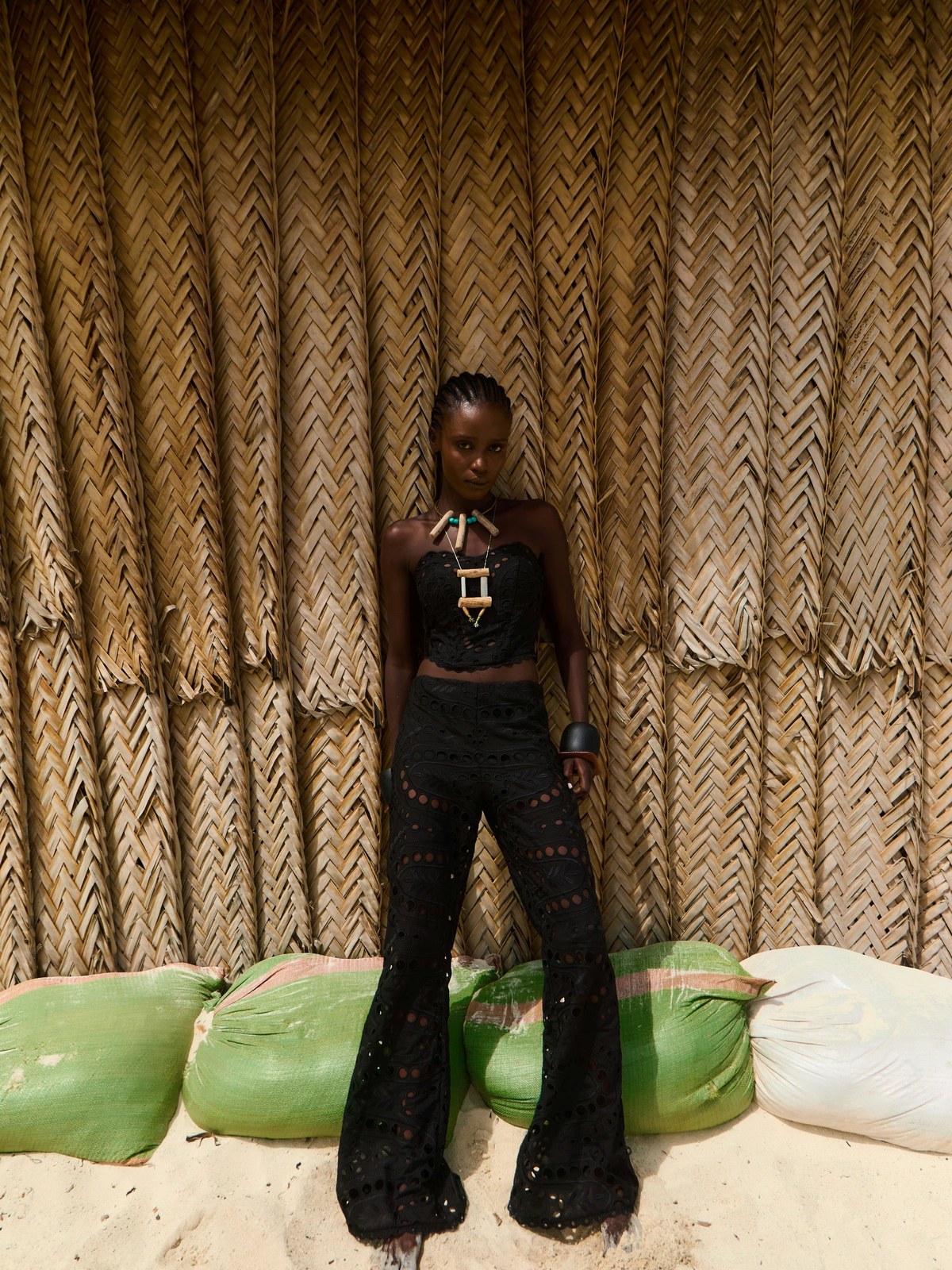 Model in a black embroidered outfit against a woven wall