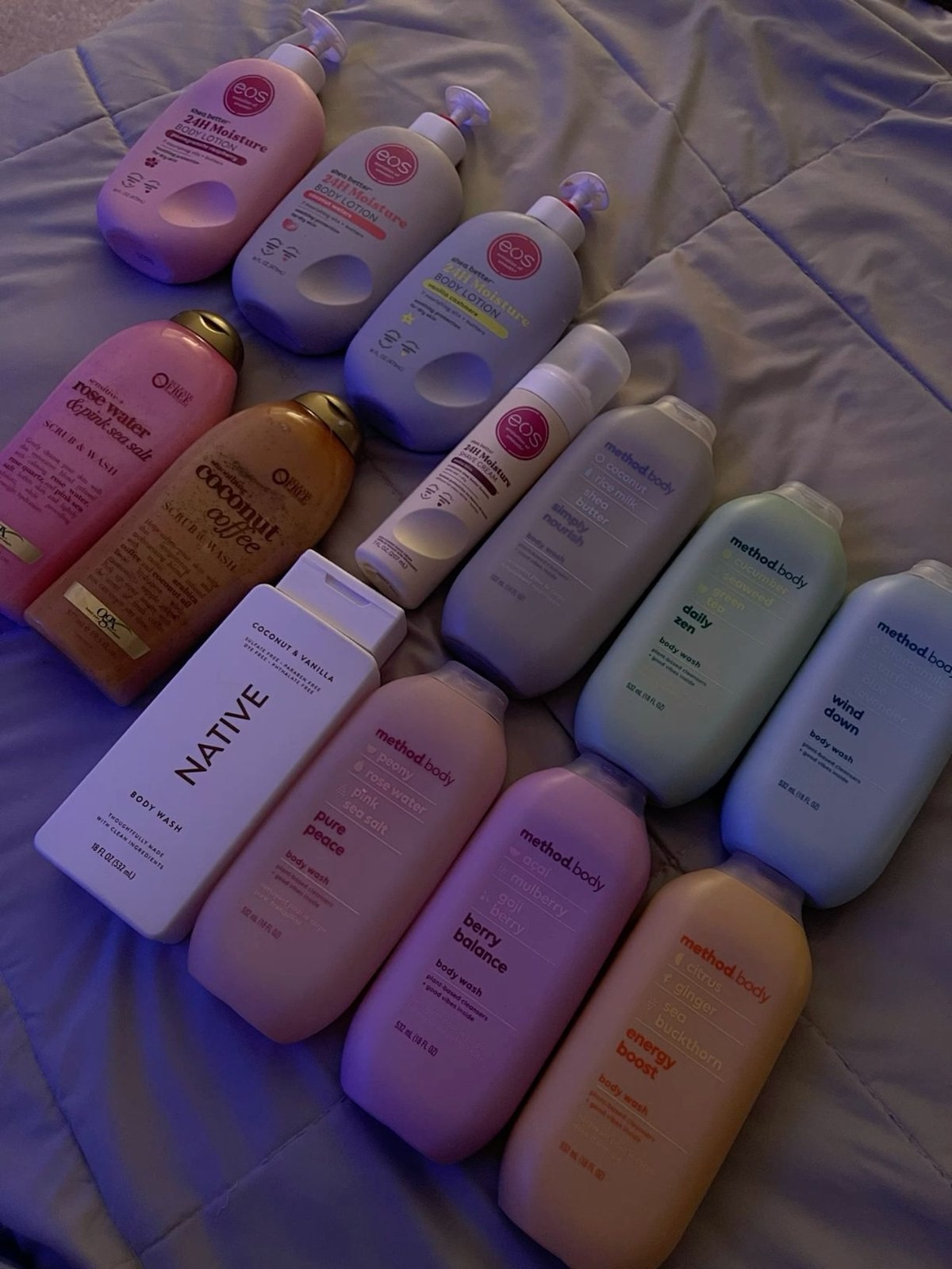 Rows of Method and other body wash and lotion bottles laid out on a bed