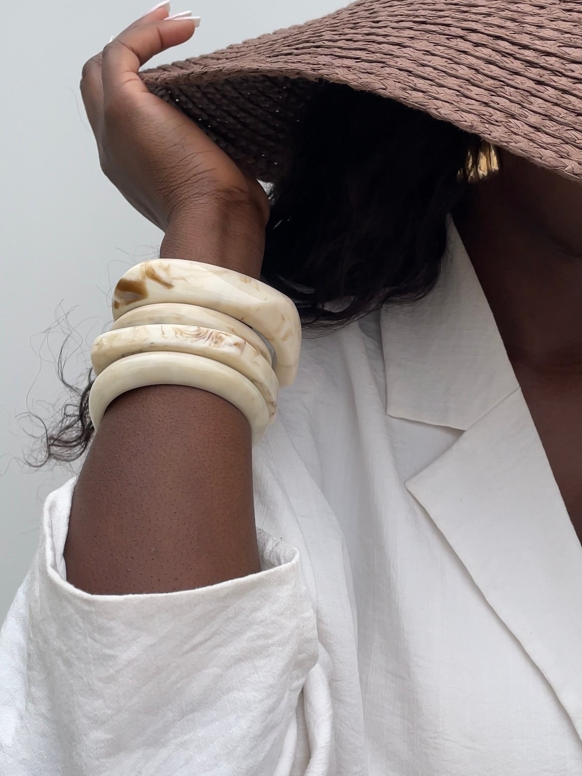 Model’s wrist stacked with marble resin bangles beneath a woven hat and white sleeve.