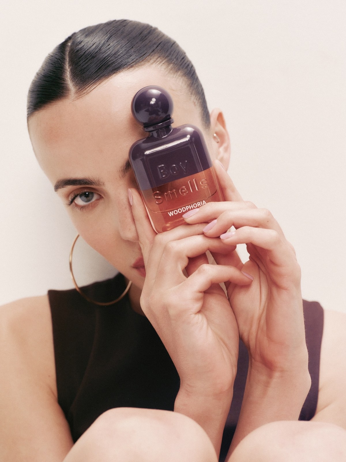 Model holding a dark Boy Smells fragrance bottle beside her face