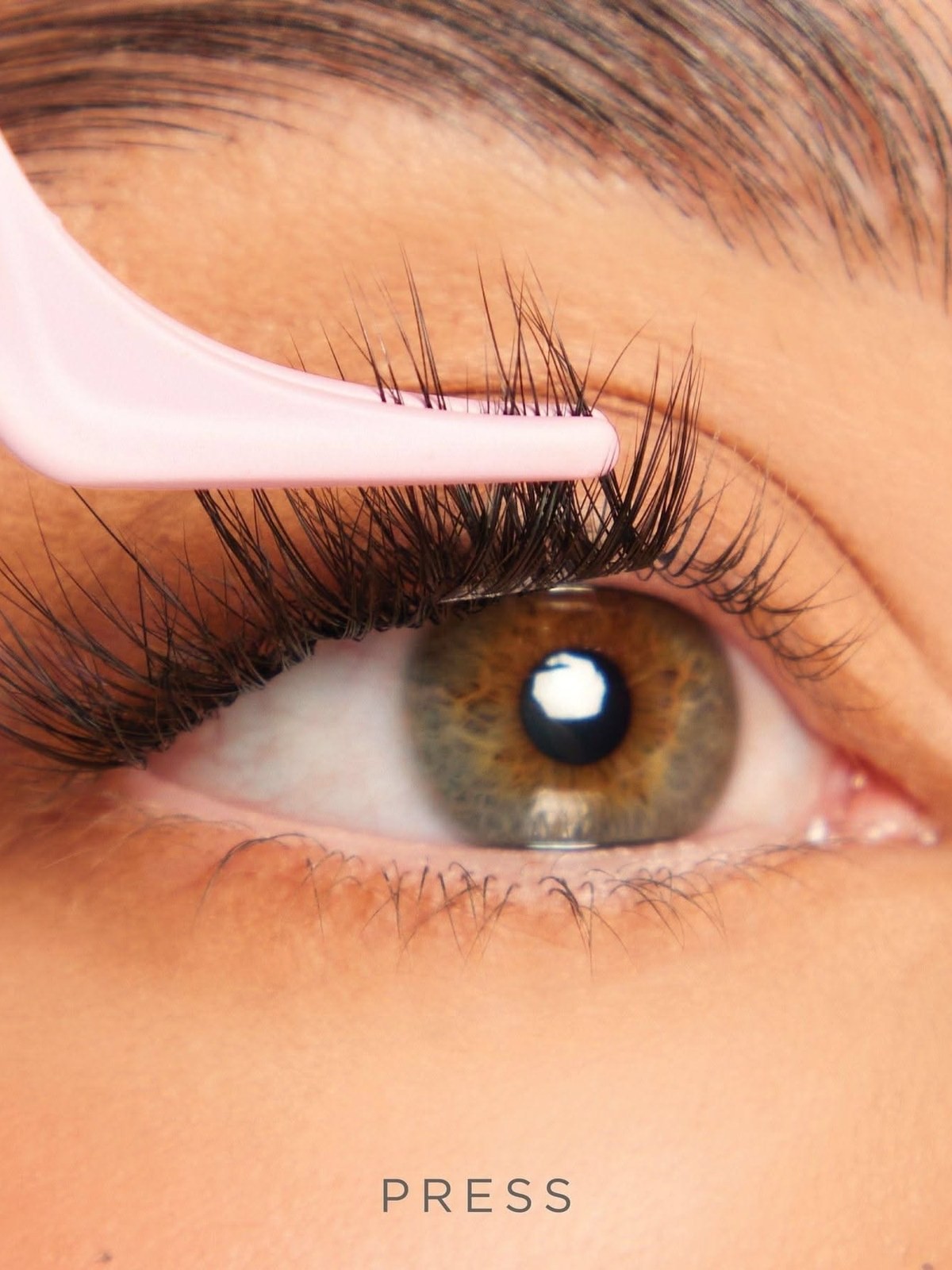Close up of a pink lash applicator pressing a cluster lash onto the lash line