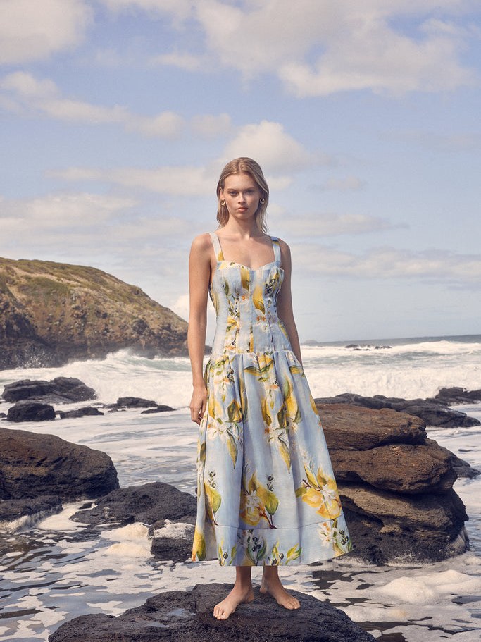 Model in a printed blue dress standing on a rocky shore