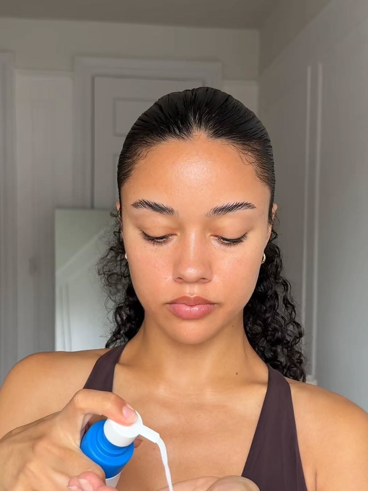 Woman with slicked-back hair pumping a white lotion from a blue-capped bottle into her hand