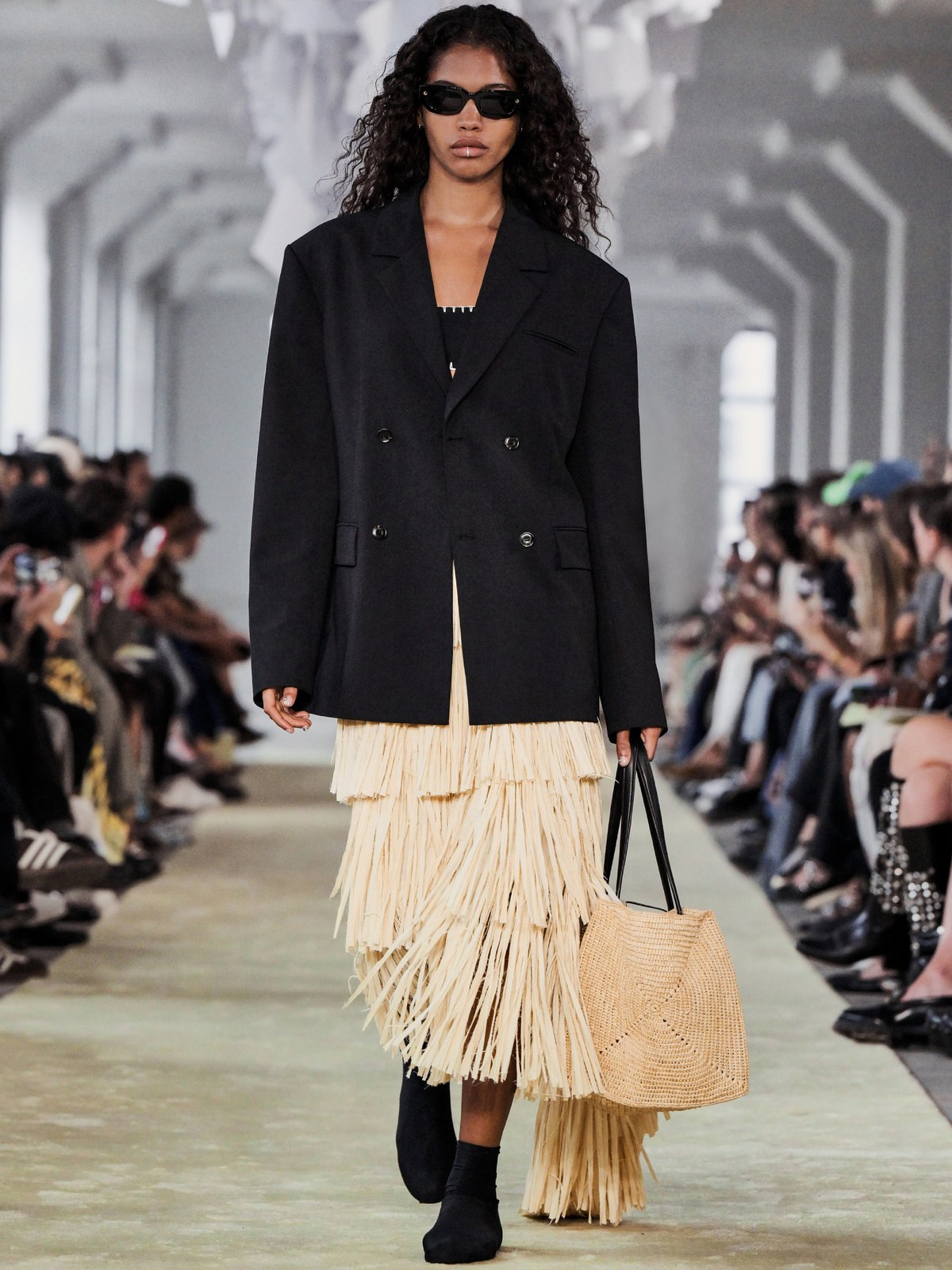 Runway model in a dark blazer and fringed skirt