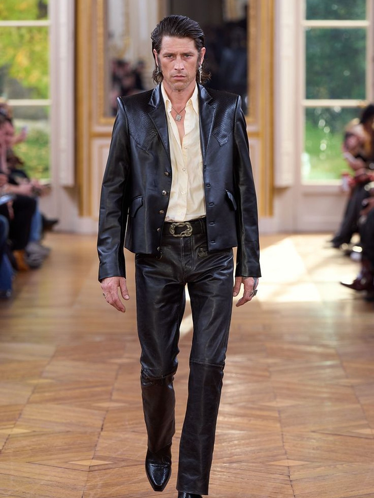 Model in a black leather jacket and trousers on a runway with parquet floors