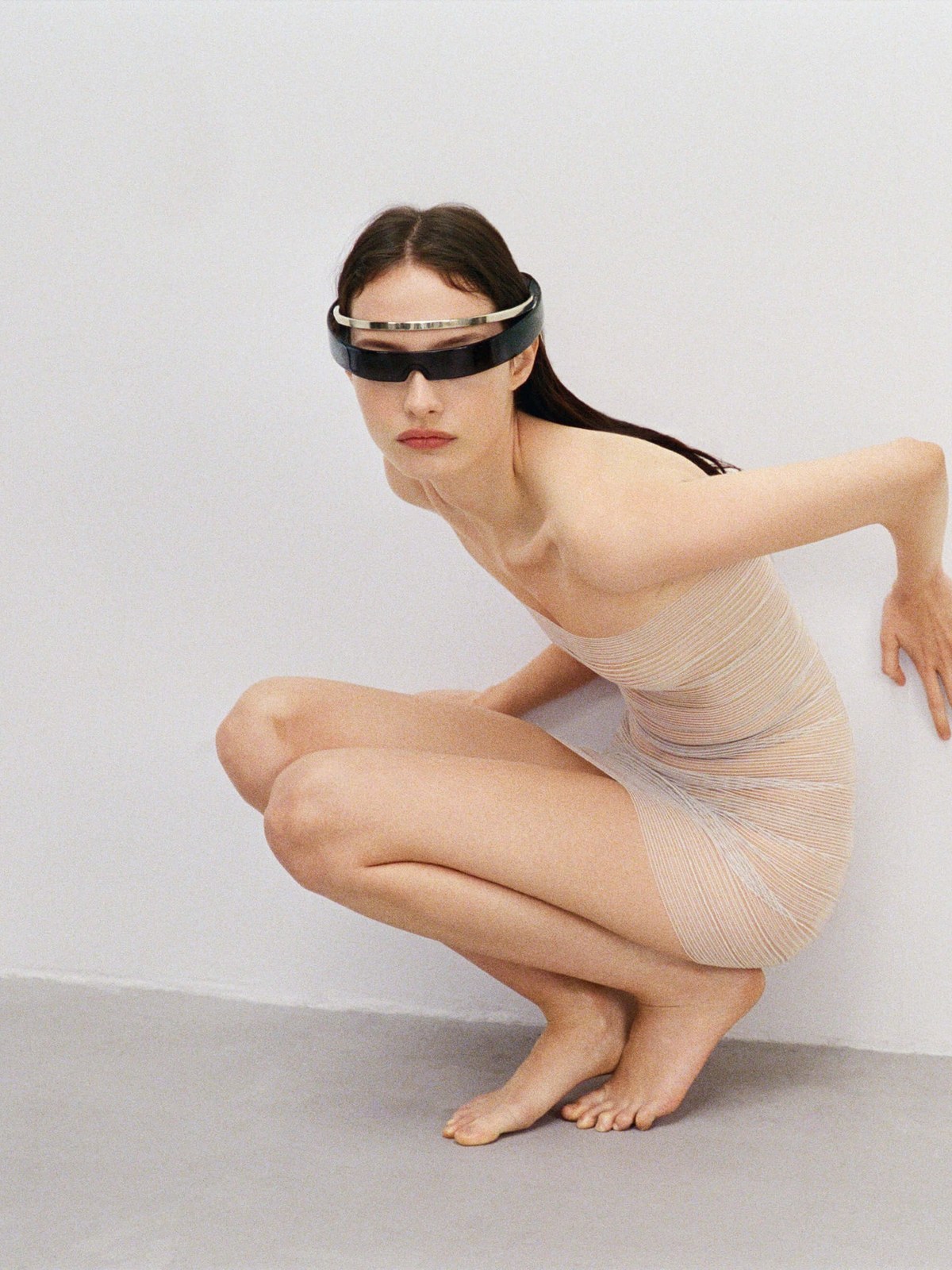 Model crouching in a sheer pale outfit and visor