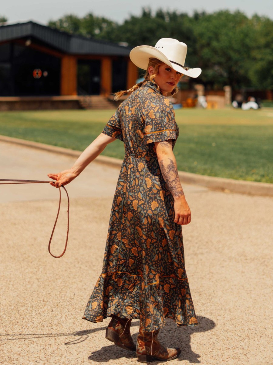 Woman in a patterned long dress and cowboy hat looking back along a Waco walkway
