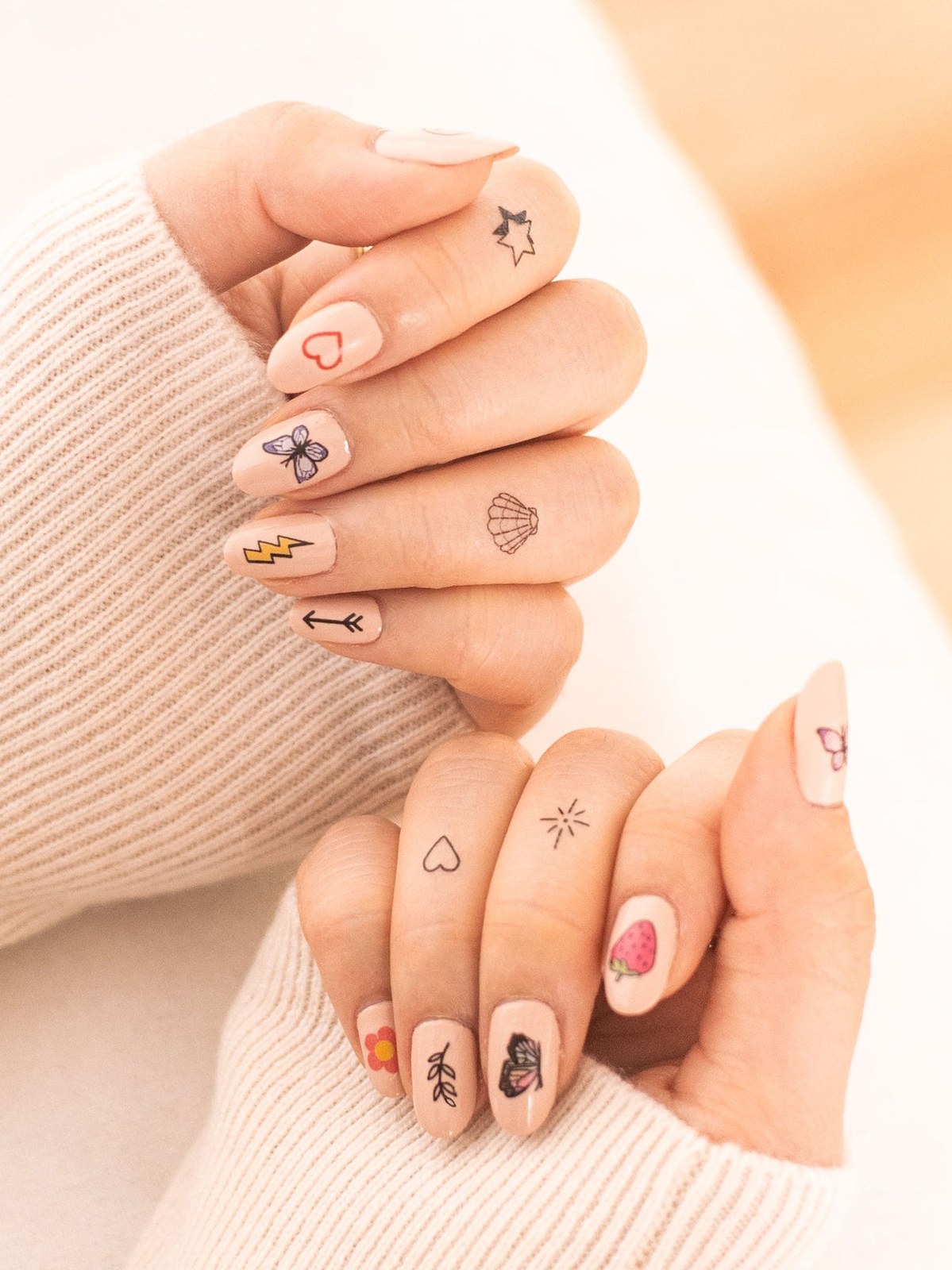 Hands in a cream knit showing small colorful nail-art tattoos