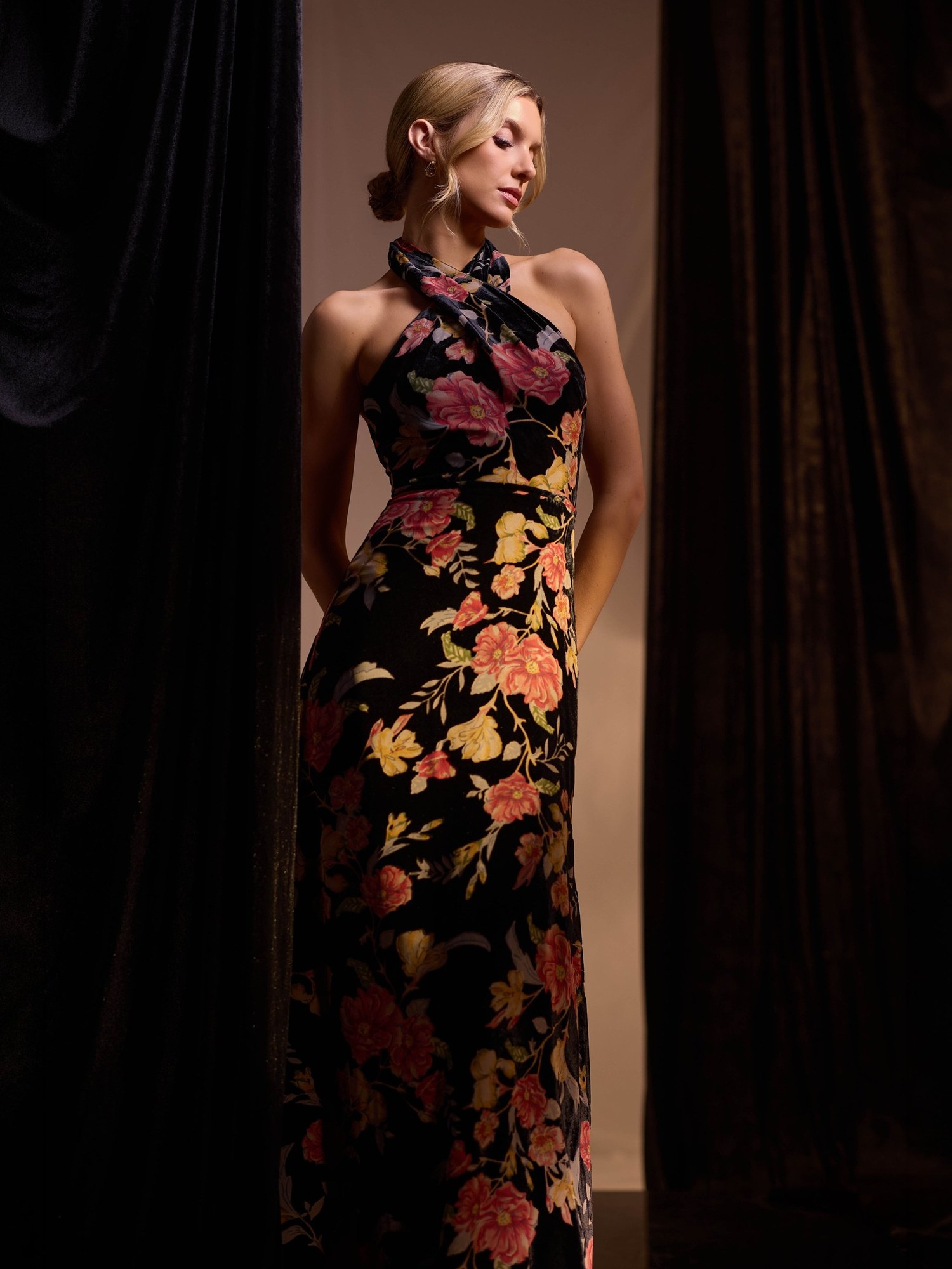 Model in a floral print halter gown between dark velvet curtains