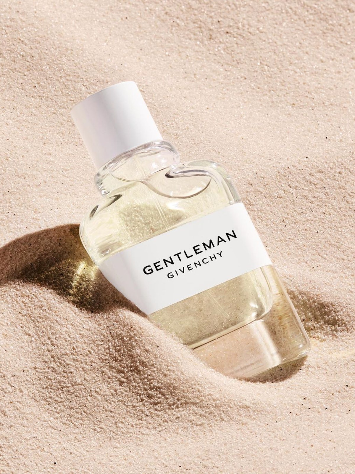 Small bottle of Givenchy Gentleman cologne resting in pale sand