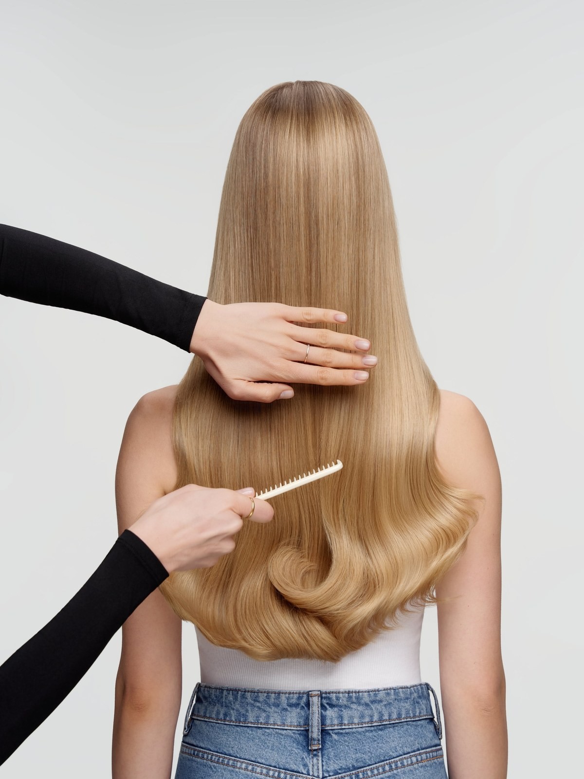 Stylist combing long straight blonde hair from behind