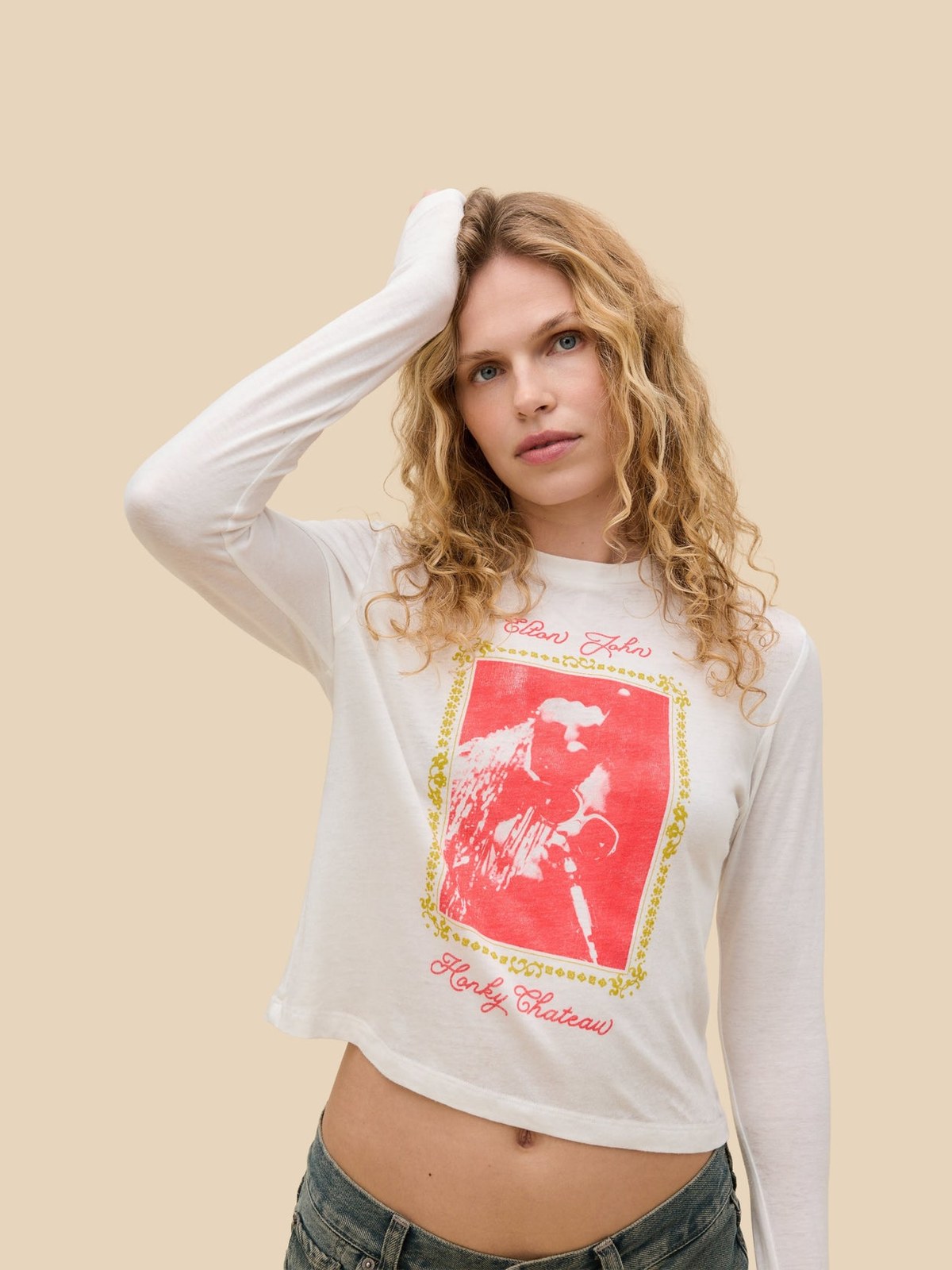 Model in a white music graphic long-sleeve tee against a warm studio backdrop