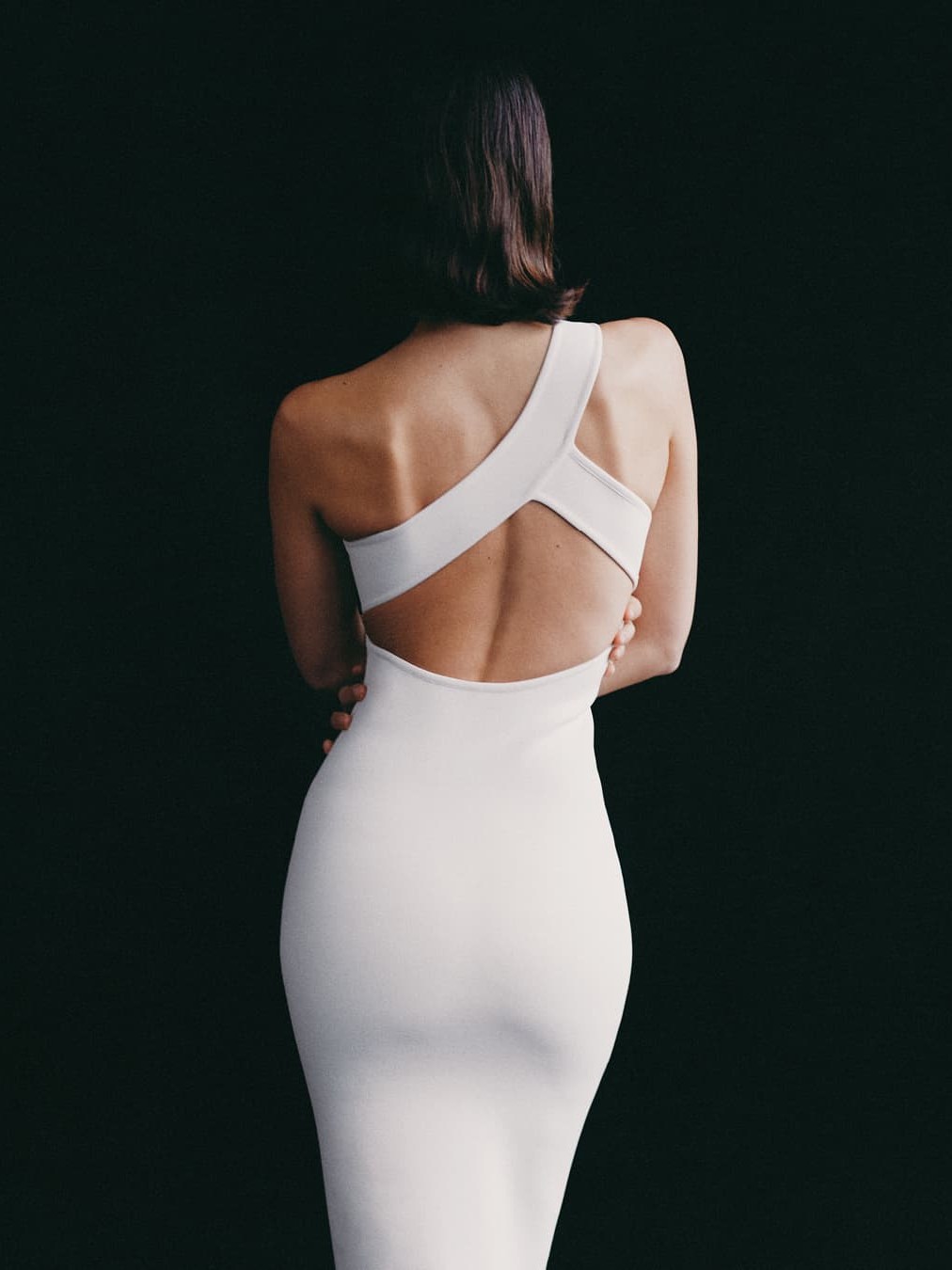Back view of an open-back white knit dress against a dark backdrop