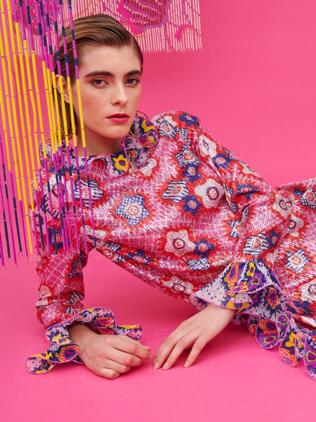 Woman in a colorful printed dress reclining against a pink studio backdrop