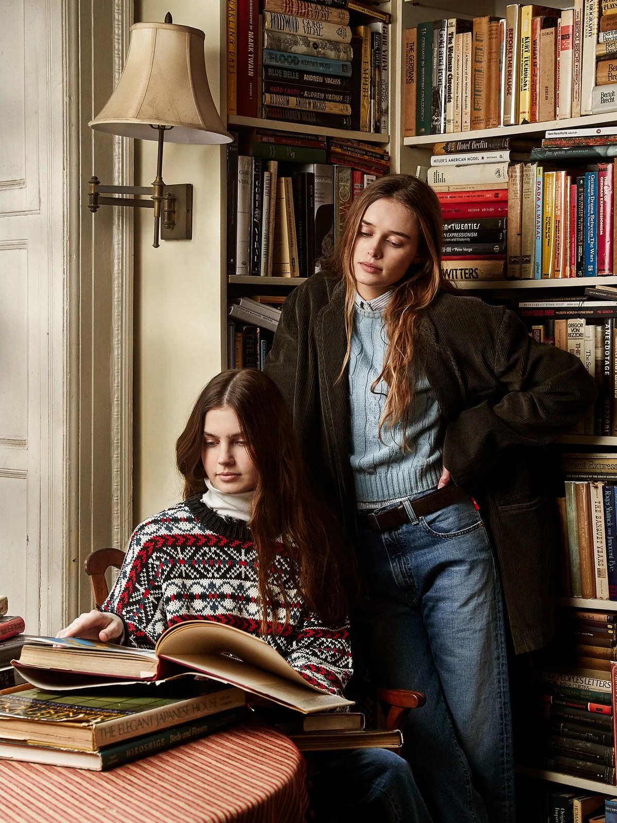 Two models in knitwear and denim reading among bookshelves in the Denimist Fall Winter campaign