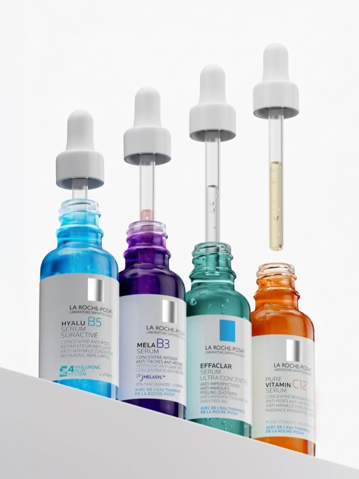 Four La Roche-Posay serums in blue, purple, green and orange bottles with their droppers lifted, Hyalu B5, Mela B3, Effaclar and Pure Vitamin C12