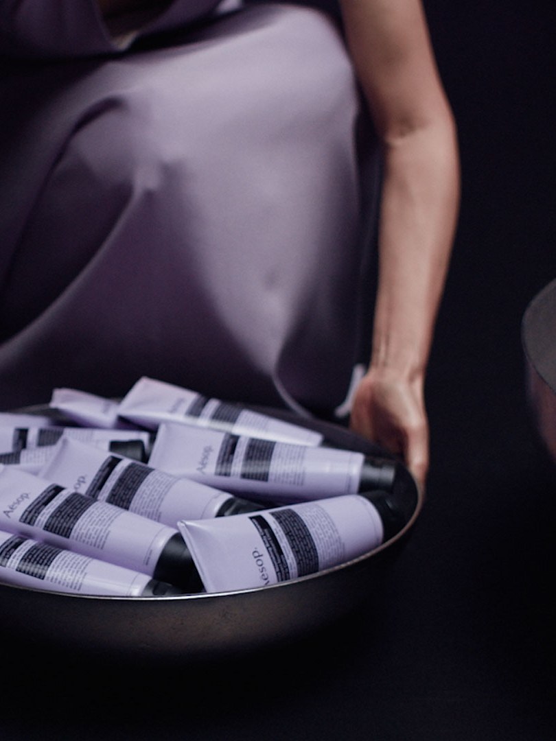 A person arranges Aesop body-care tubes beside a sculptural basin
