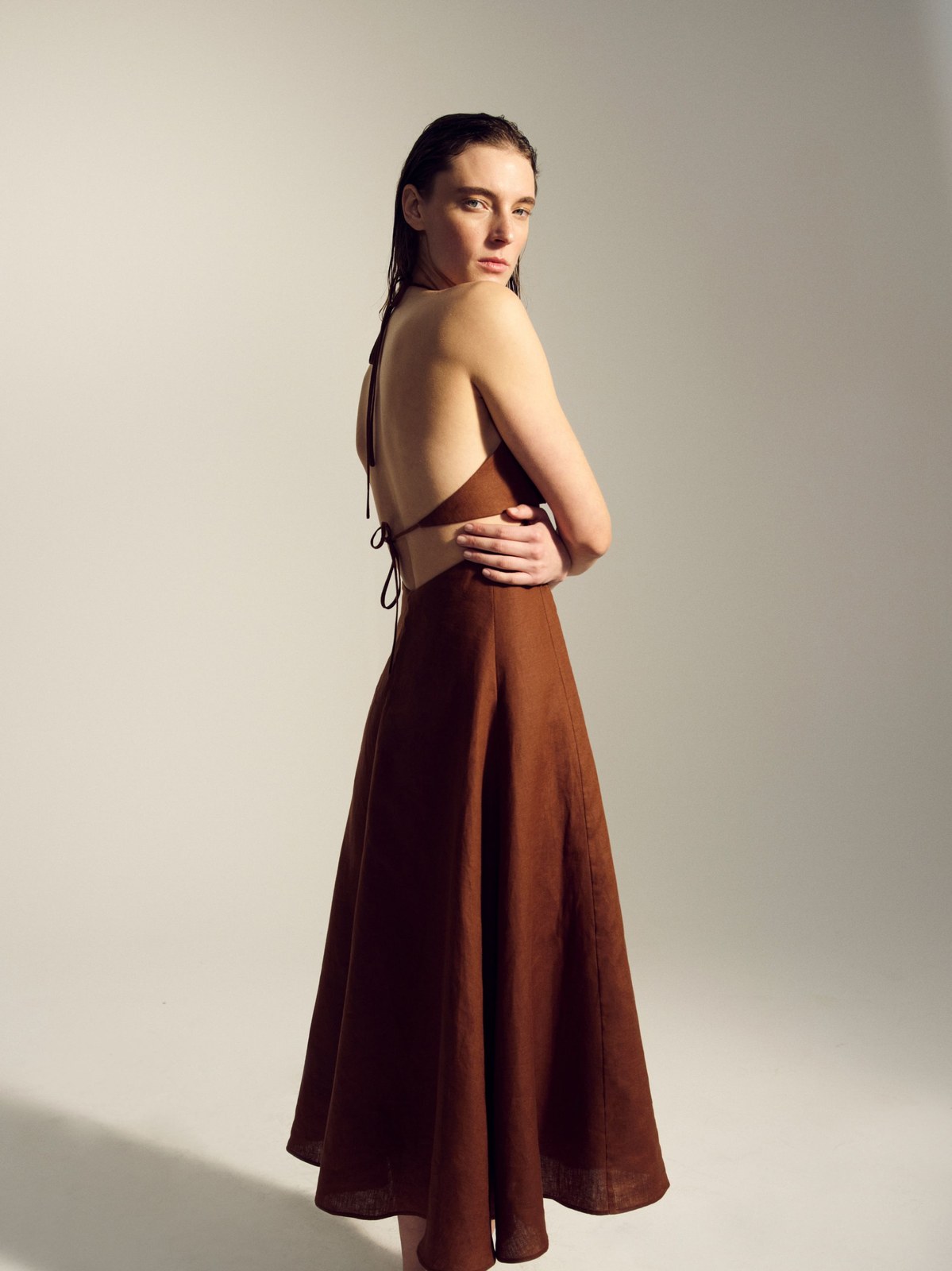 Model in a long burgundy dress, turning to look back against a pale studio backdrop