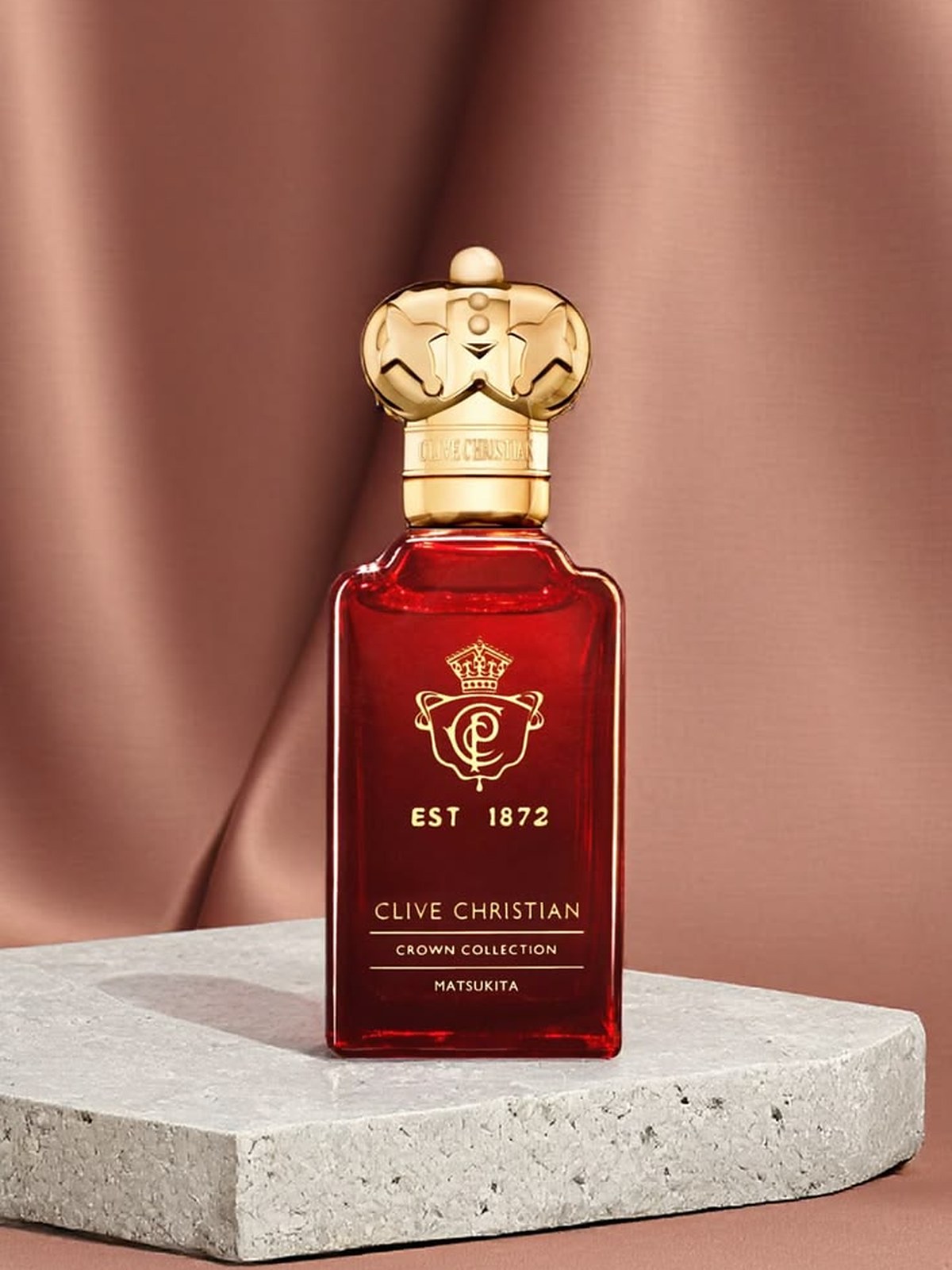 Red Clive Christian crown bottle on a pale stone block against a pink backdrop