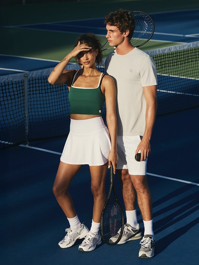 Woman in a tennis skirt and tank with another player on court