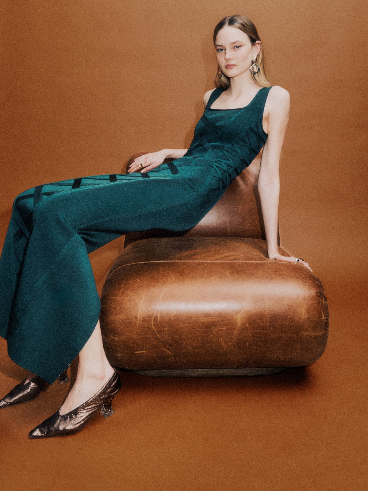 Woman in a teal evening gown seated beside a tan ottoman