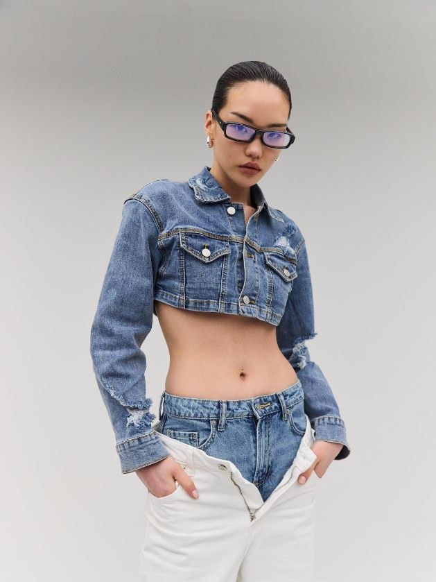 Model in blue-light frames, a cropped denim jacket, and white trousers