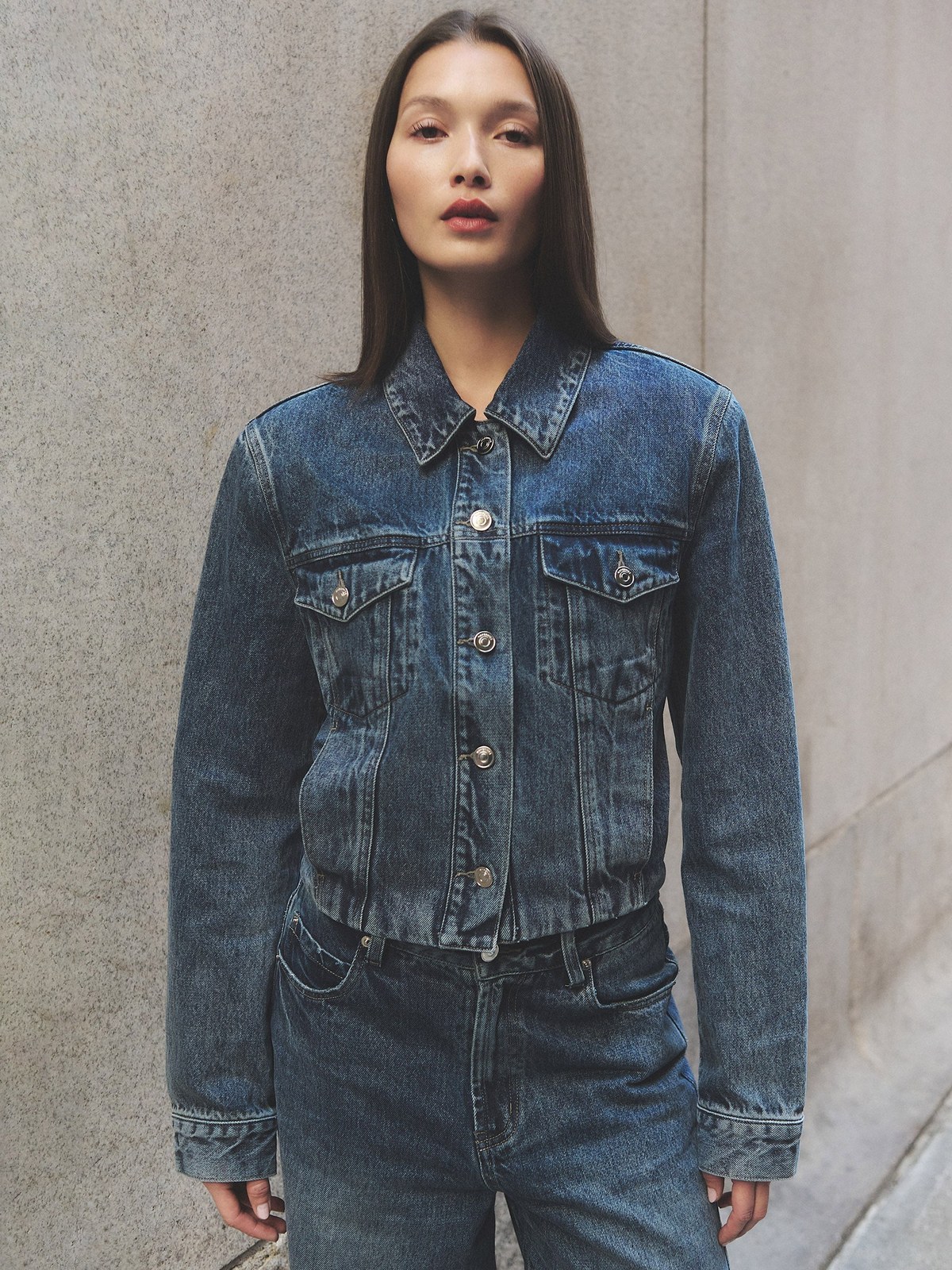 Model in a denim jacket and jeans against a concrete wall