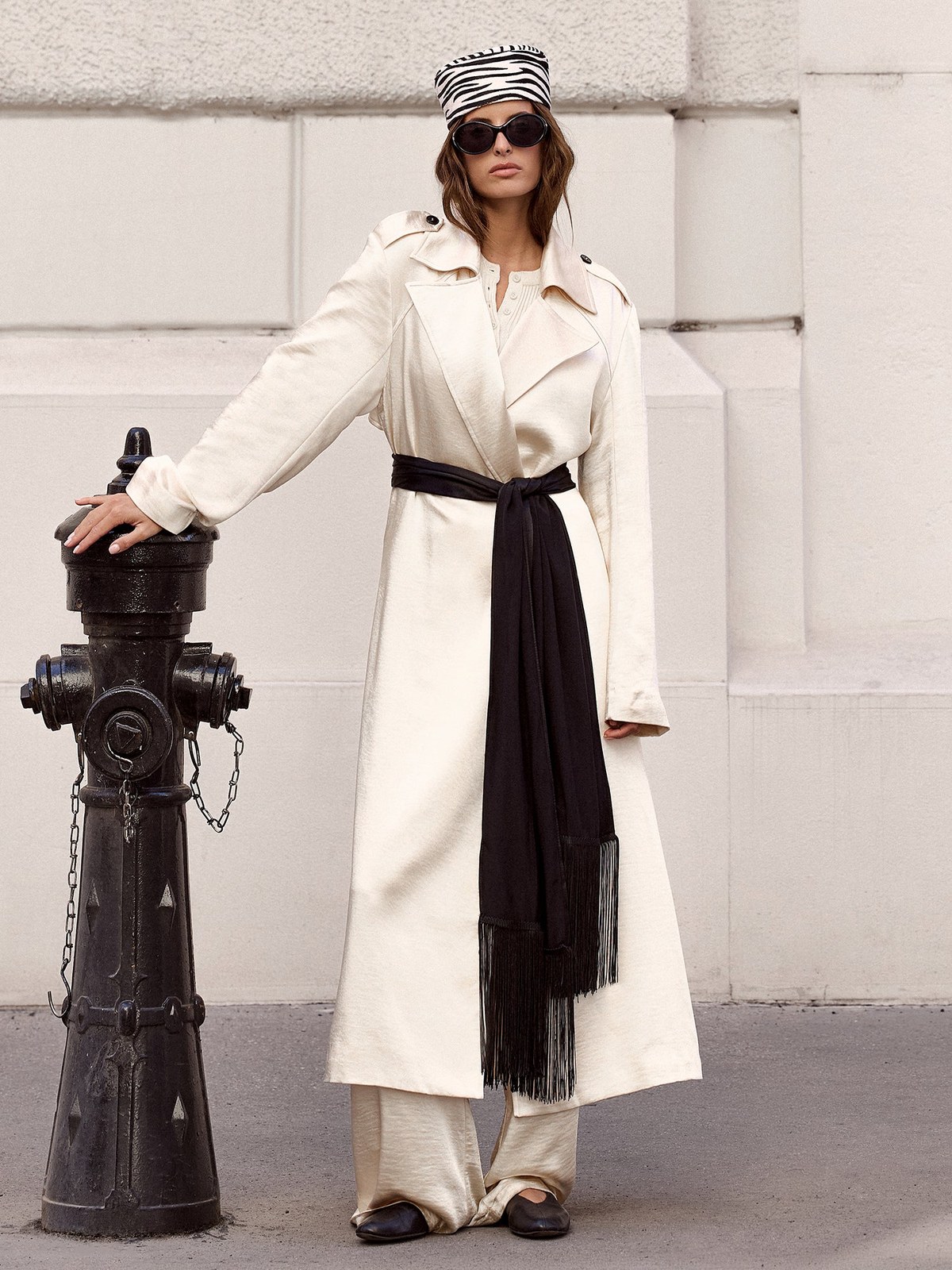 Model in a light trench and white trousers beside a city fire hydrant