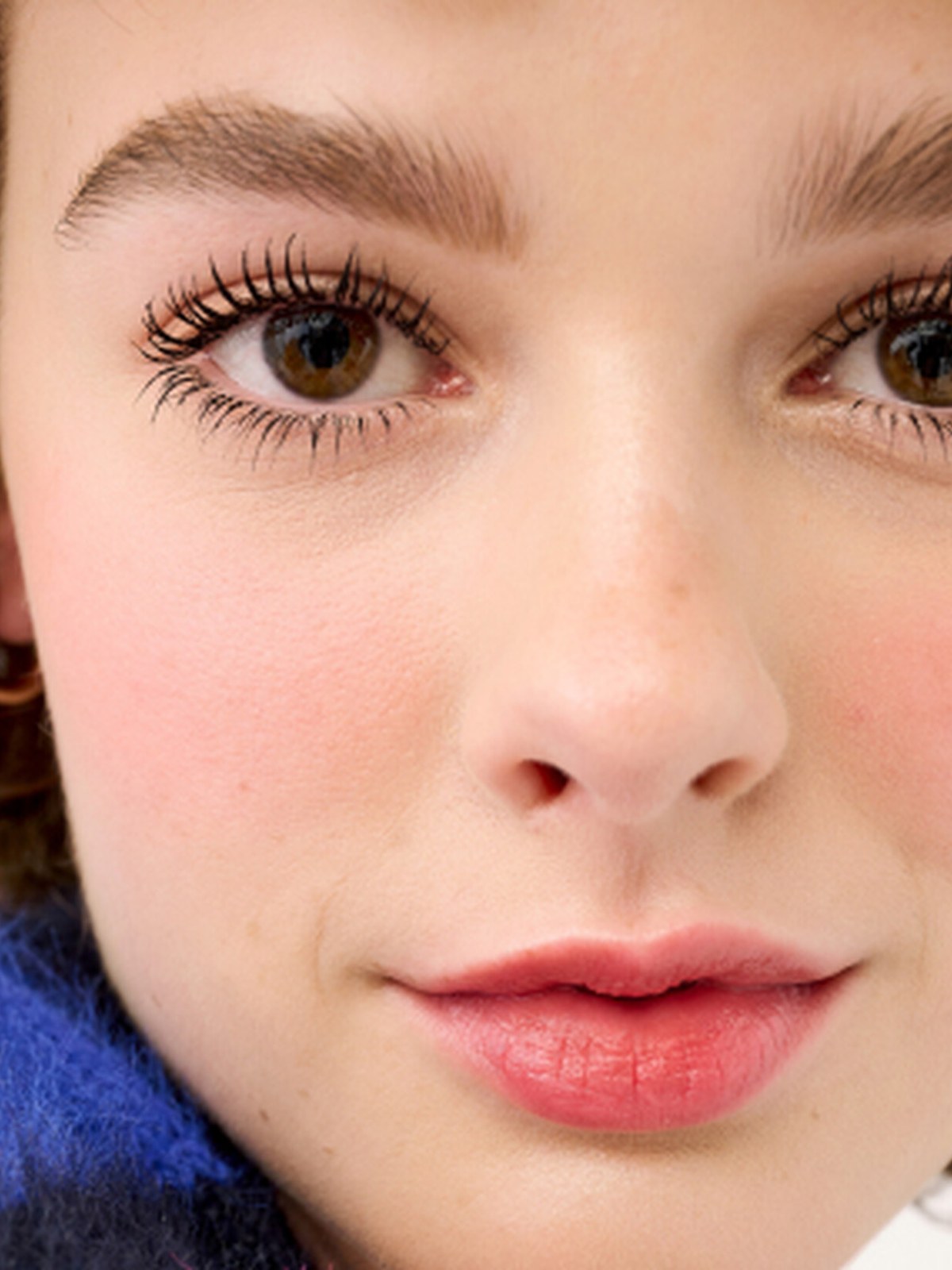 Curly haired woman with soft pink blush and lip in a blue knit