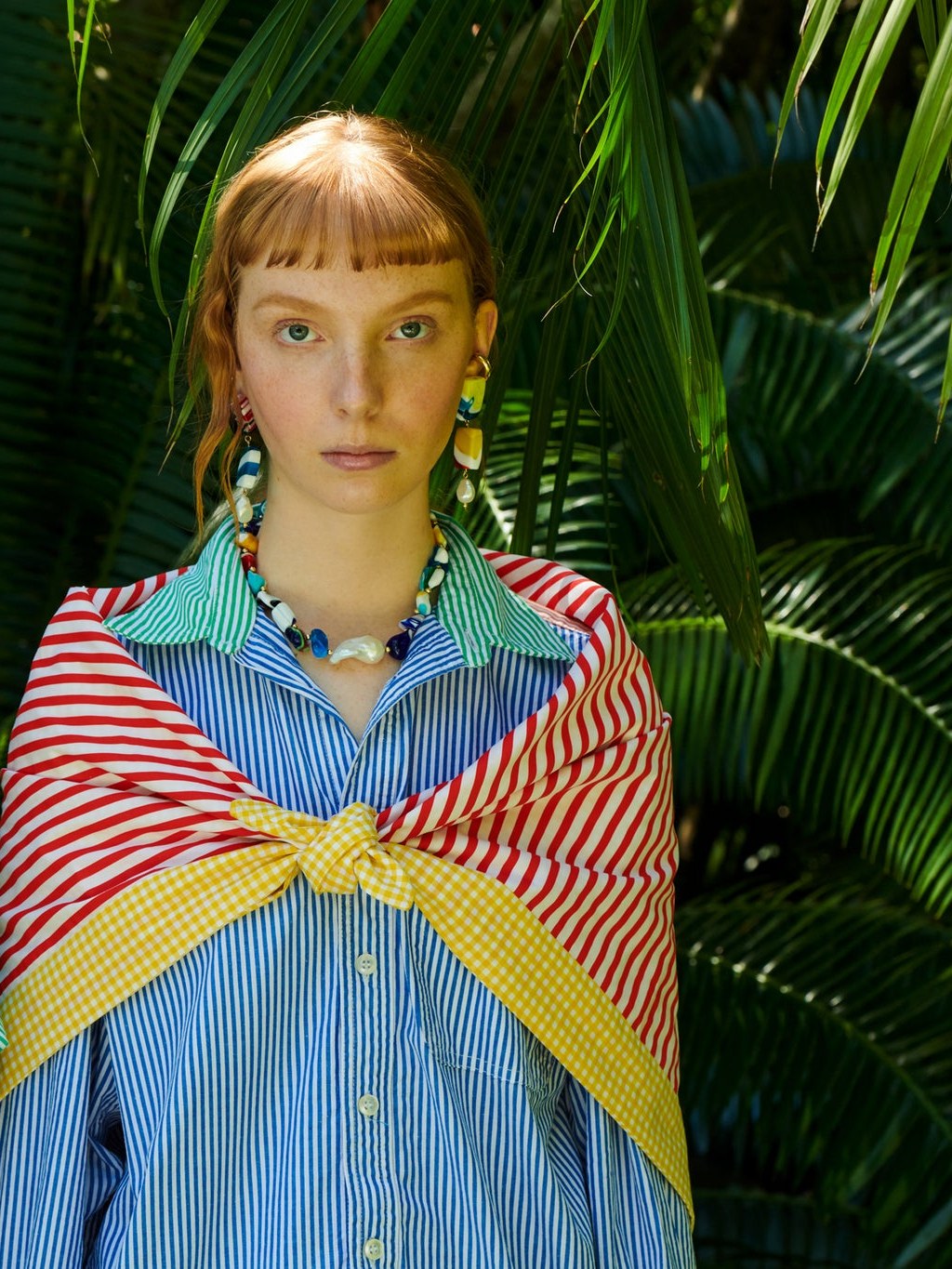 Model in colorful jewelry and striped clothing against tropical foliage