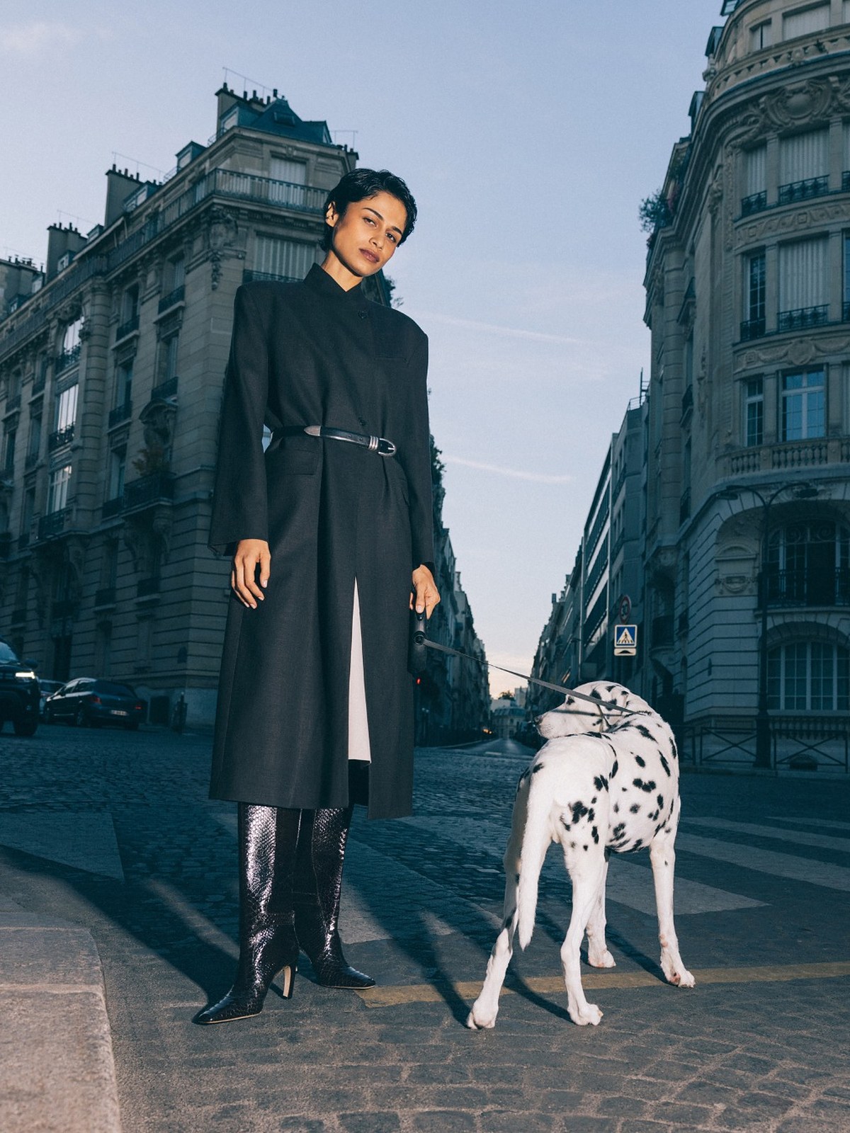 Woman in a black belted coat and tall boots with a Dalmatian on a Paris street