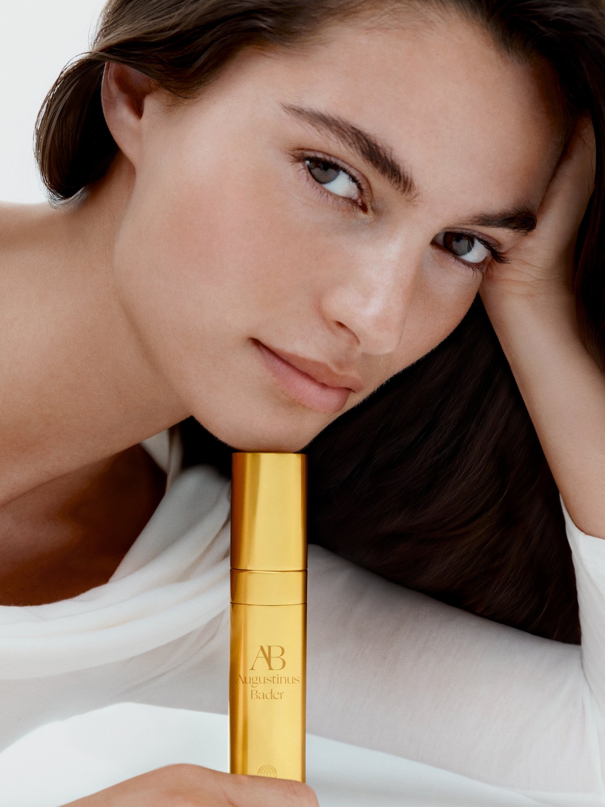 Woman with dark hair resting beside a gold serum bottle
