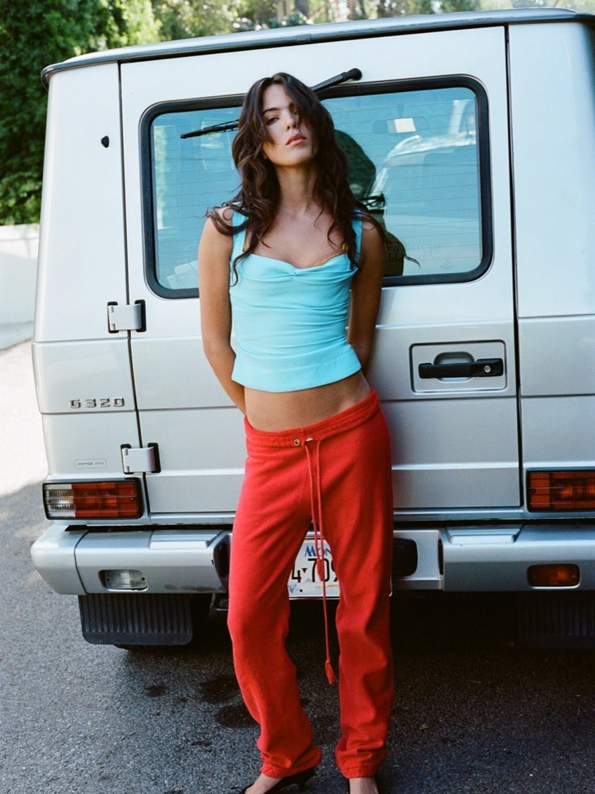 Miaou model in a blue tank and red trousers beside a vehicle.