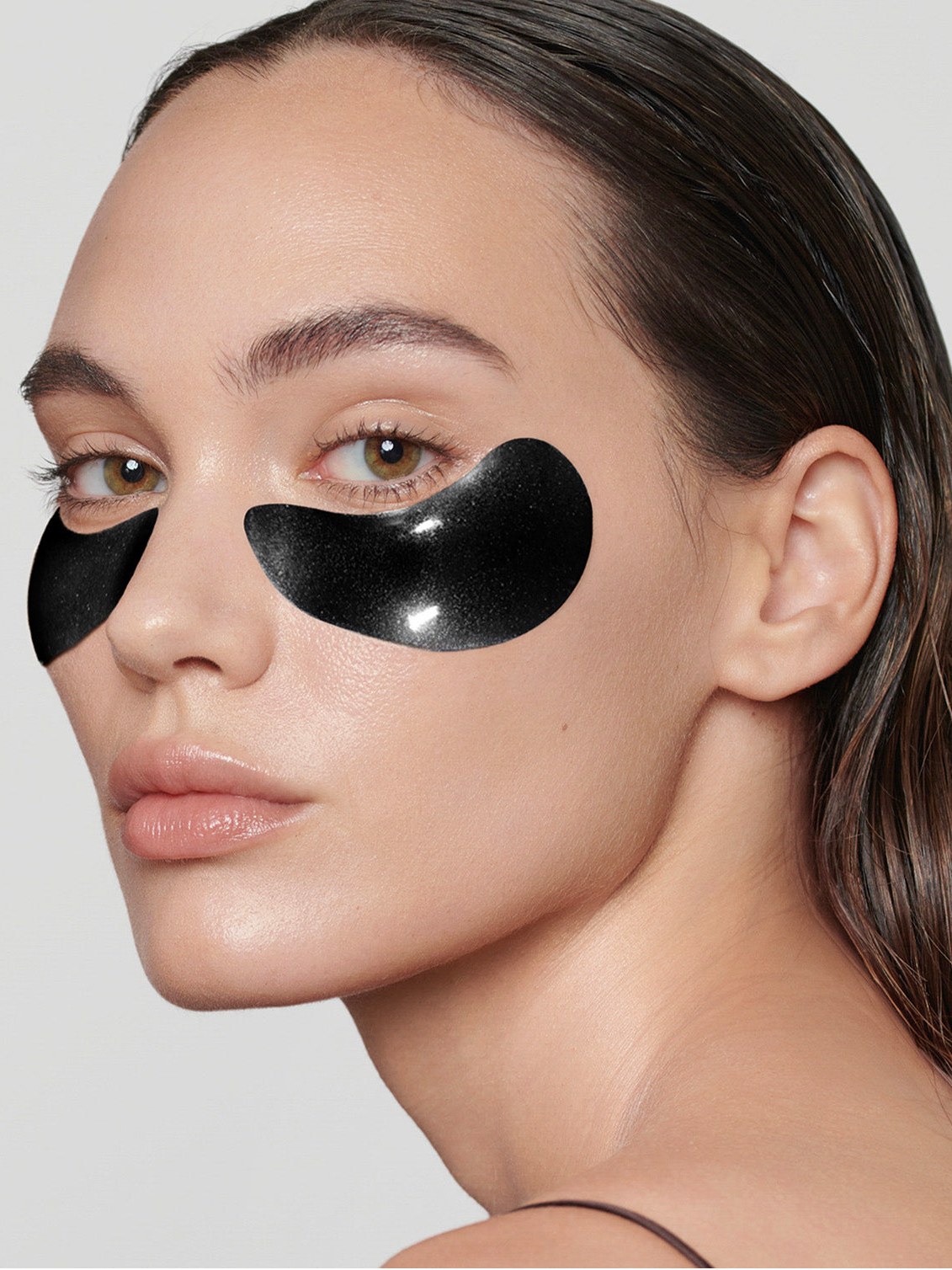 Model wearing black under-eye patches in a clean studio portrait