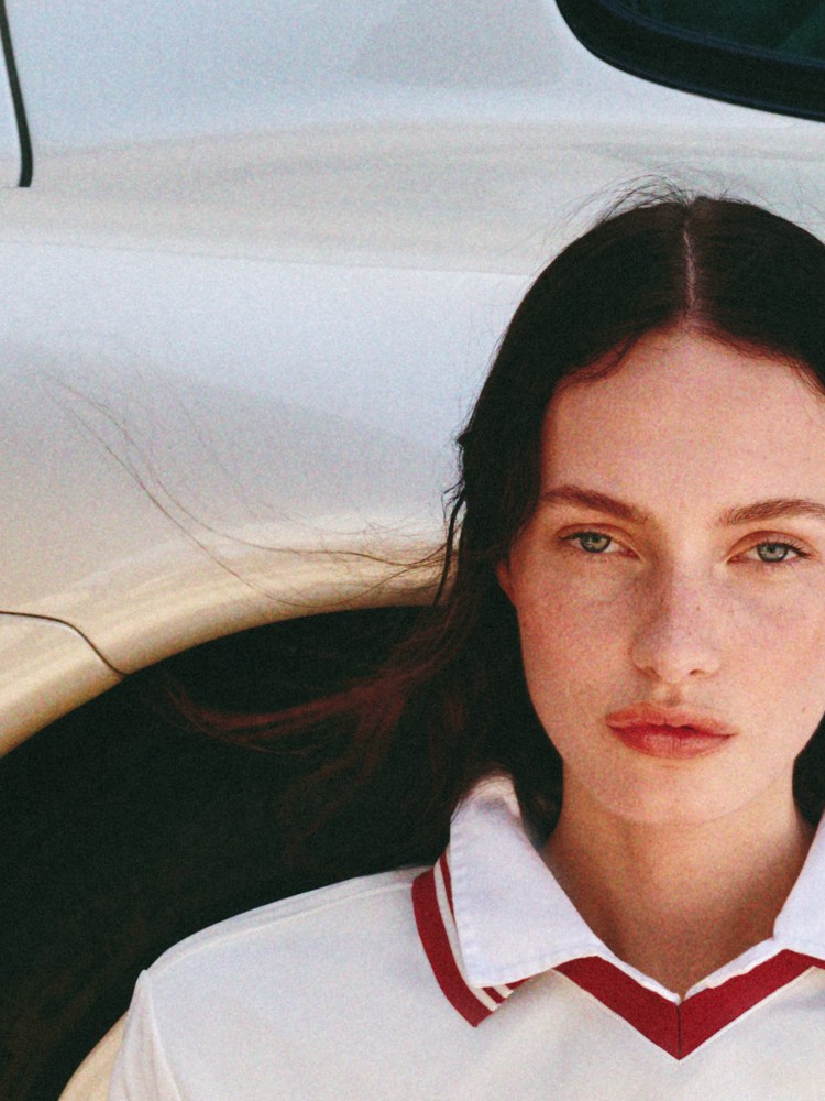 Close portrait of a model in a white racing-style top beside a sports car