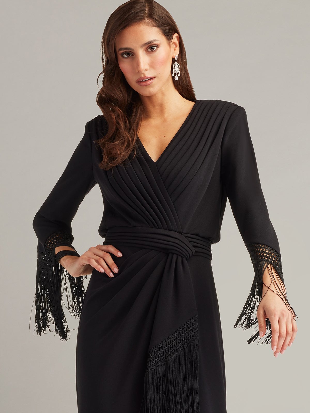 Model in a black wrap dress with fringed cuffs on a grey backdrop