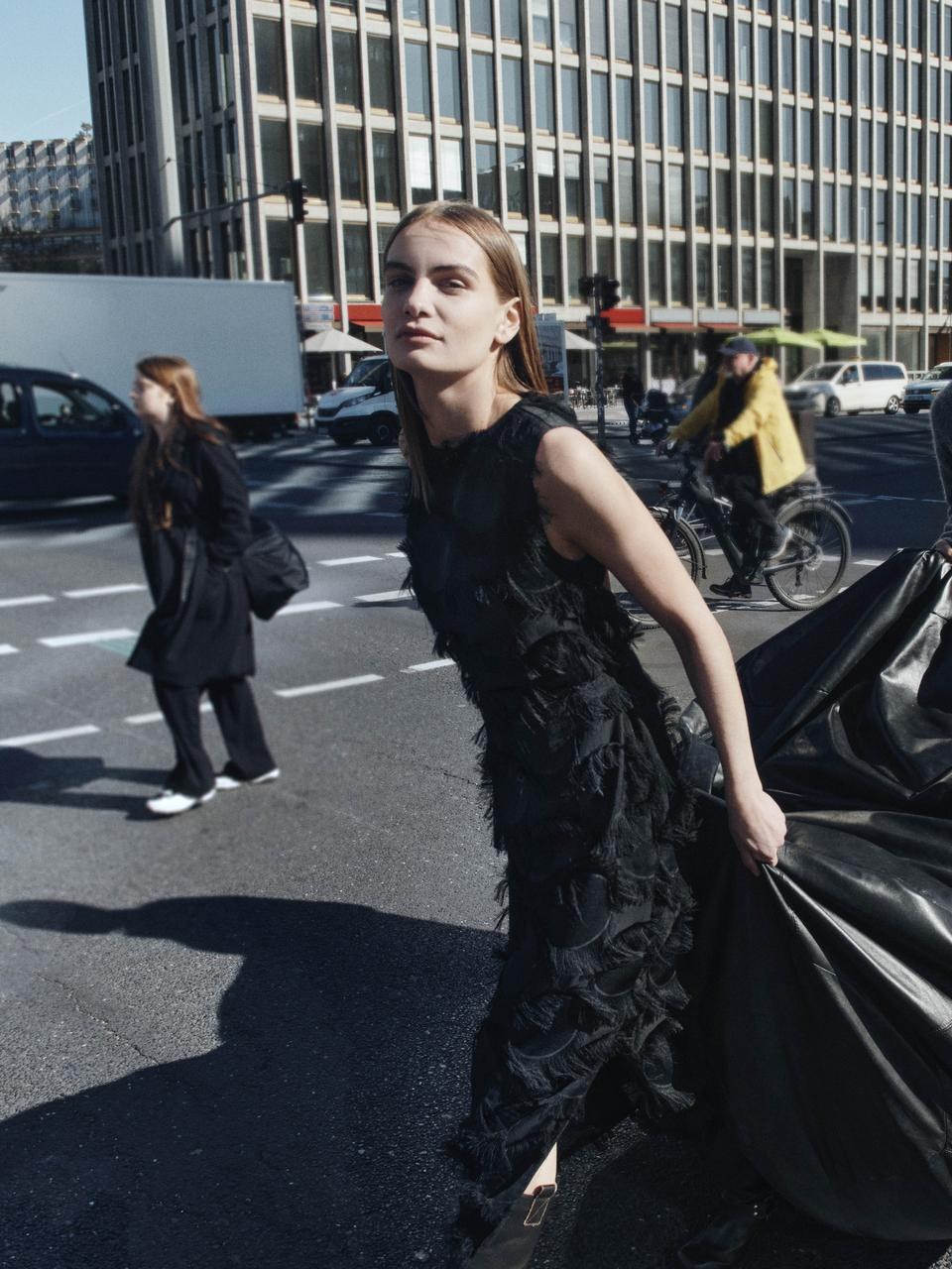 Woman in a sculptural black dress crossing a city street with a sweep of black fabric