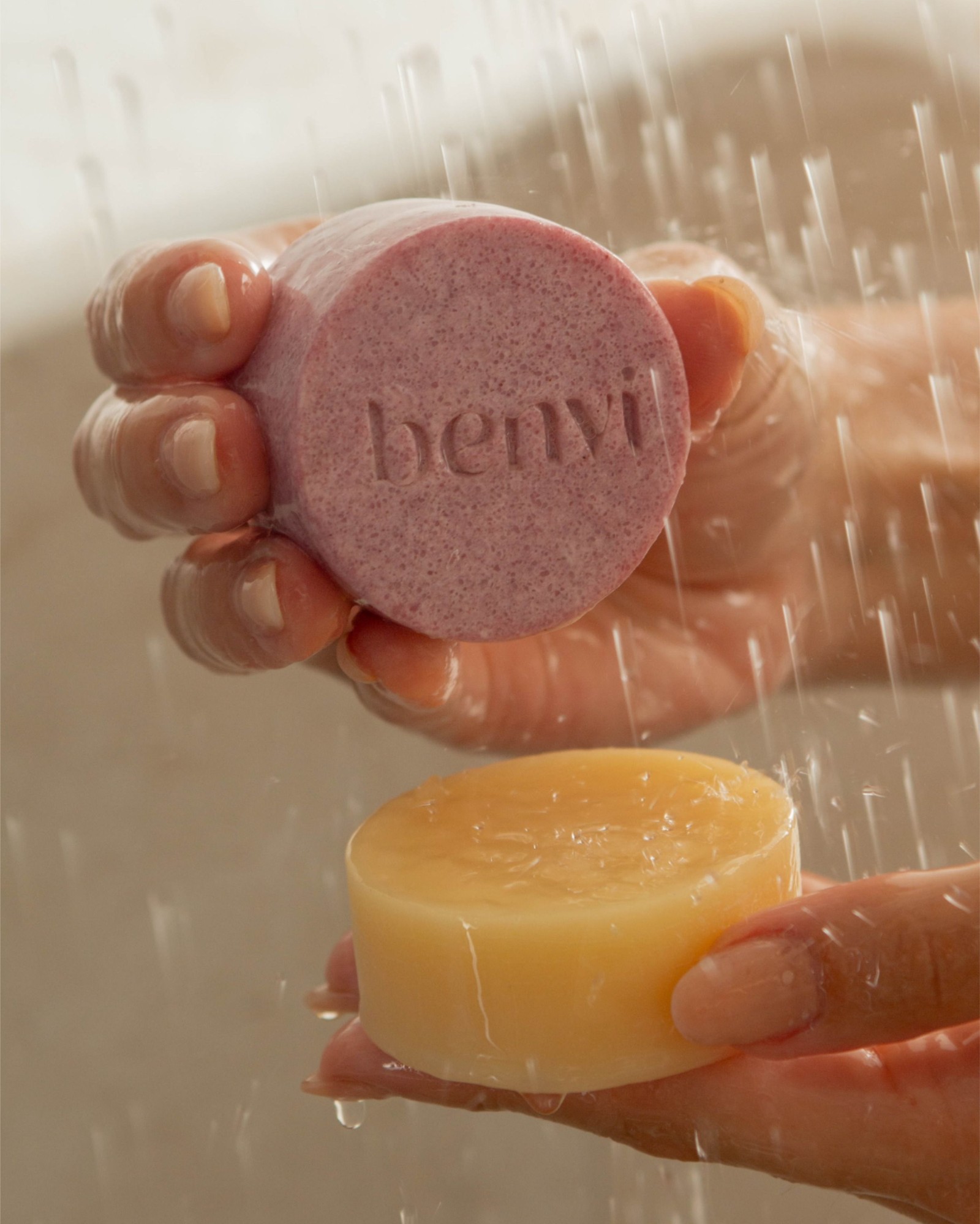 Hands holding a round pink solid bar and a yellow bar under falling shower water