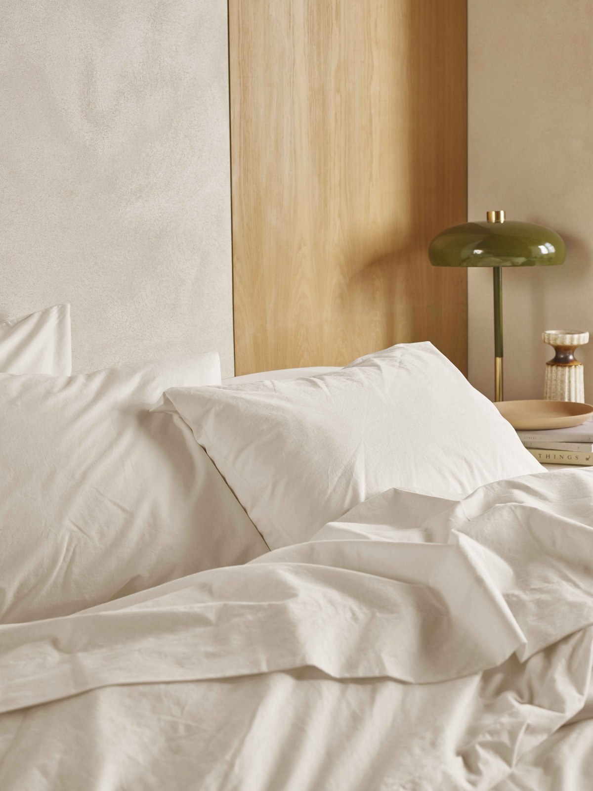 Neutral bedroom with cream bedding, a light wood panel and an olive green lamp on the nightstand