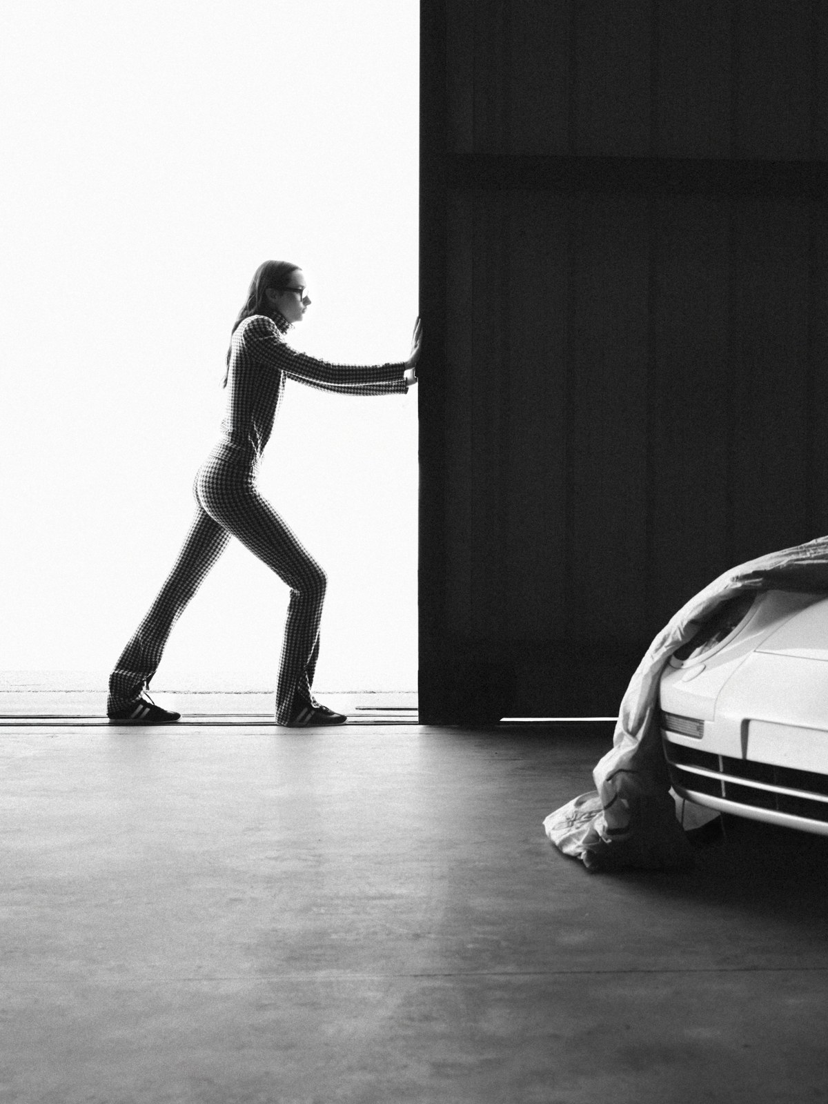 Black-and-white campaign scene with a figure beside a Porsche sports car