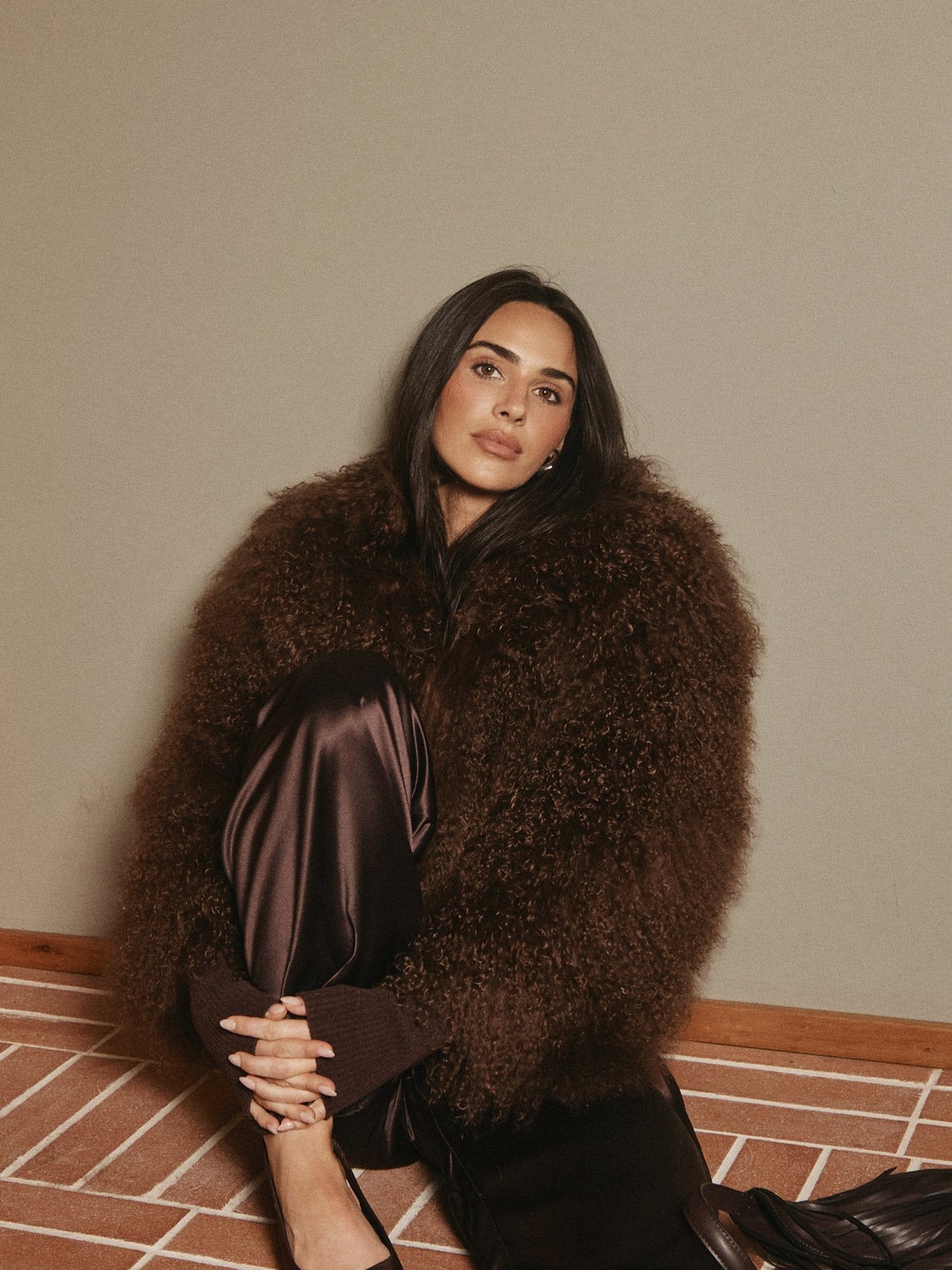 Model in a deep brown fur jacket seated on a tiled floor