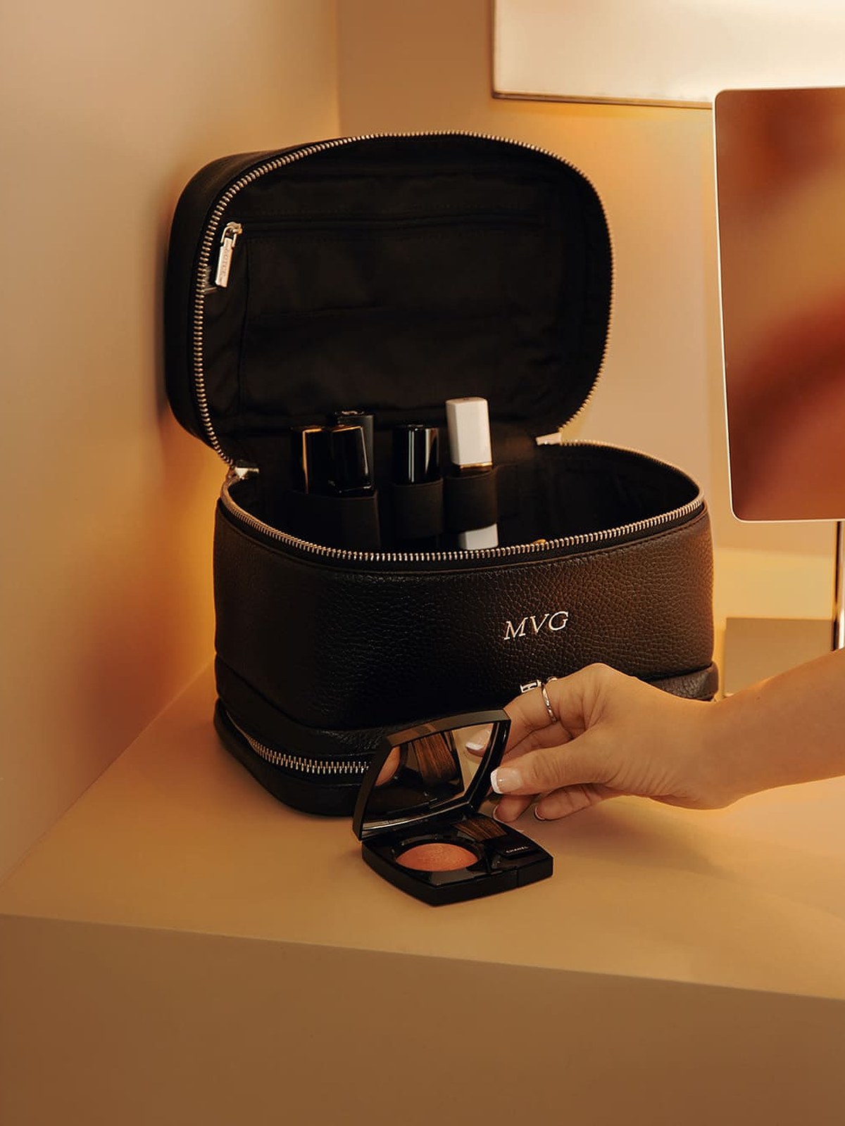 Hand reaching into an open black leather cosmetic case on a lit vanity