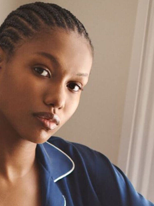 Model in a navy sleep shirt with white piping, pictured close to a vase of blue flowers