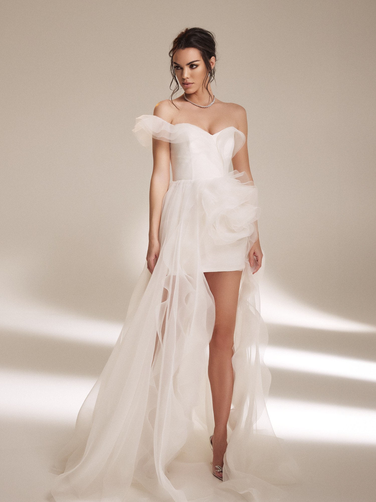 Model in an off shoulder white mini dress with an asymmetric tulle ruffle overlay