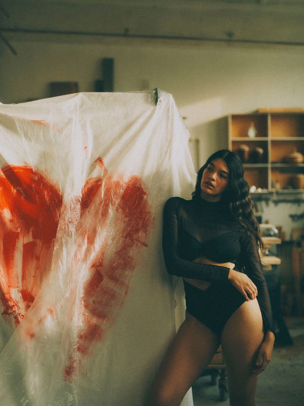Model in black lingerie posing beside a large painted canvas
