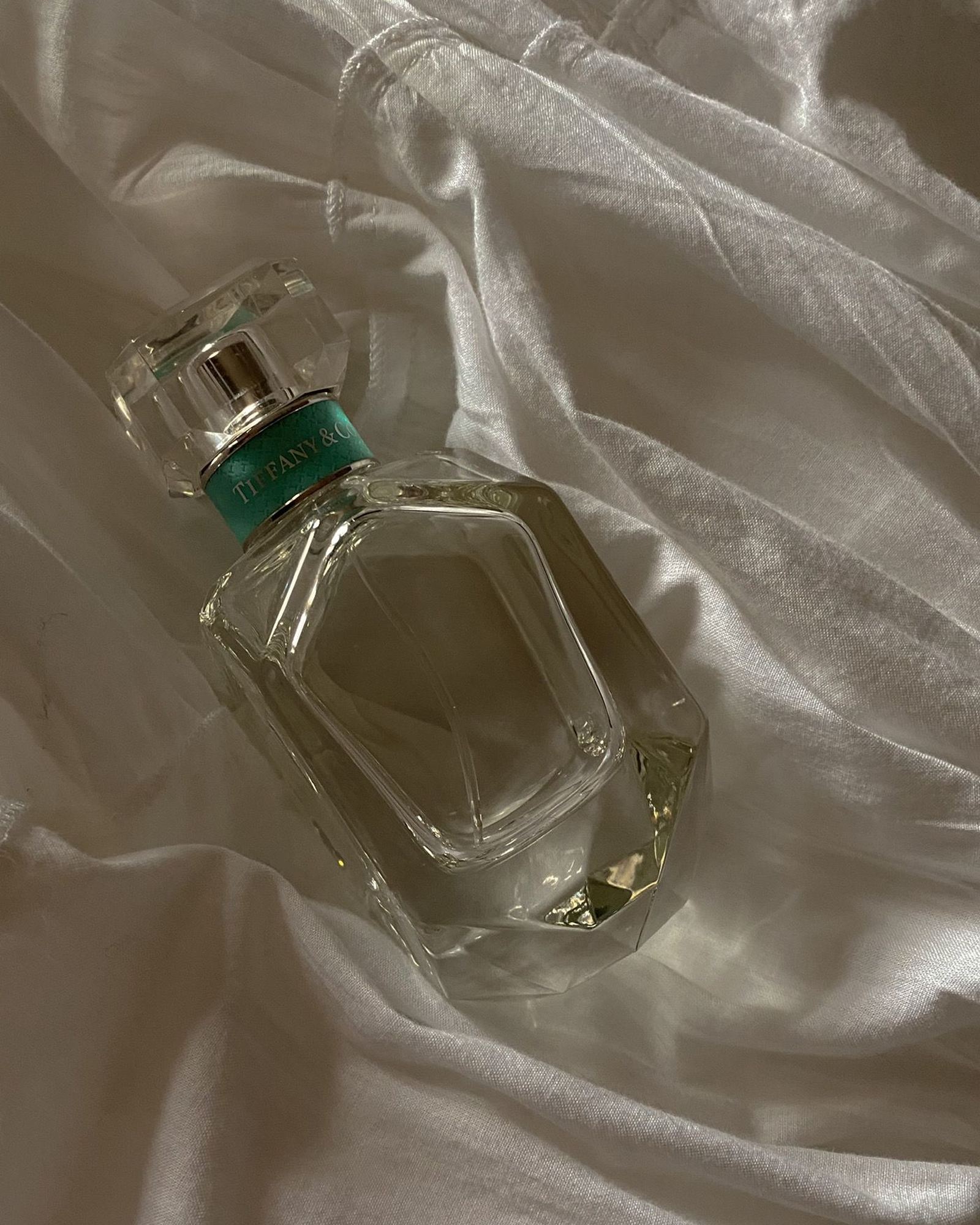 Faceted Tiffany & Co. perfume bottle with a blue collar lying on rumpled white linen